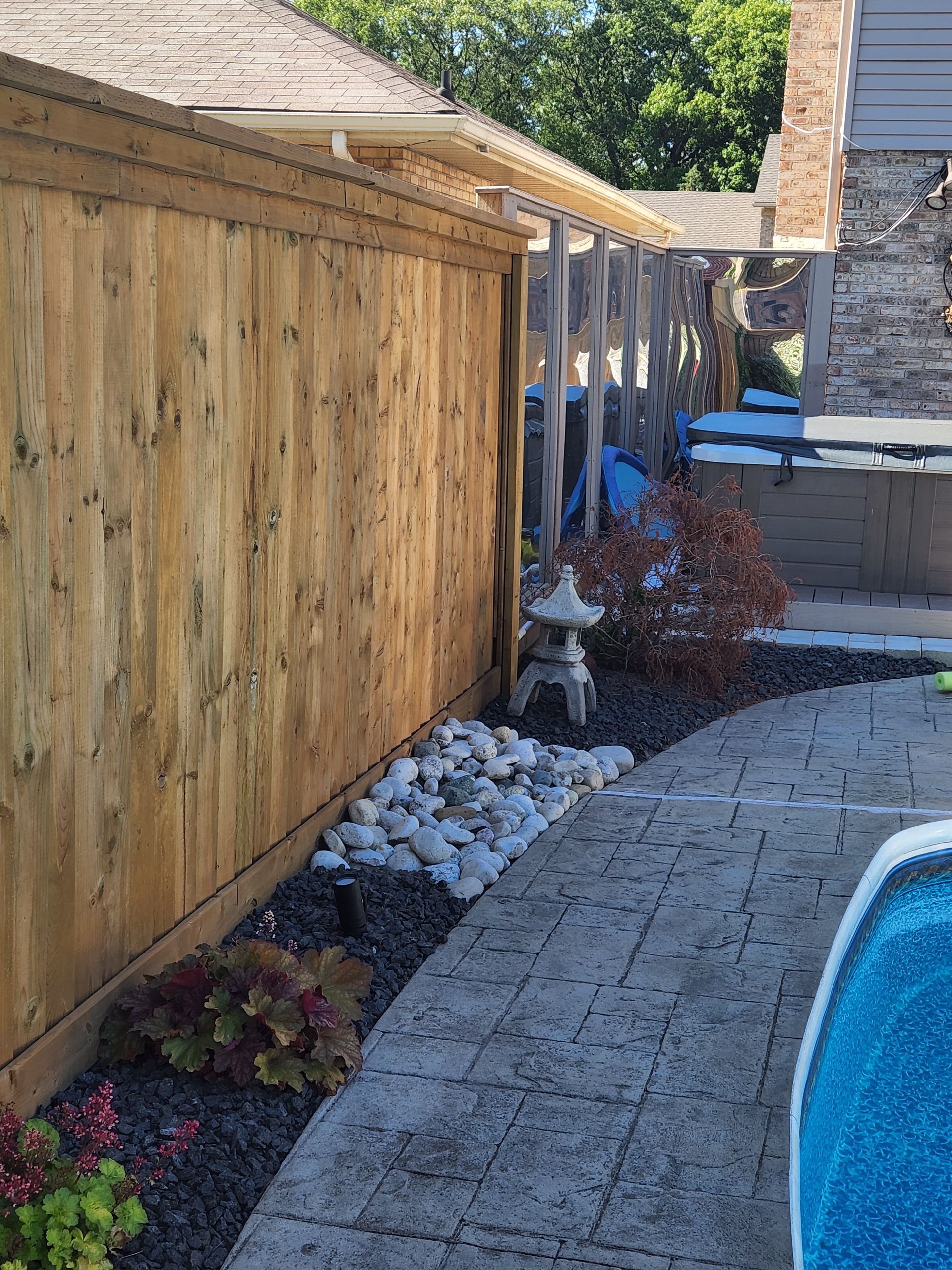 Wooden fence with decorative rock border and stone path leading to a pool.