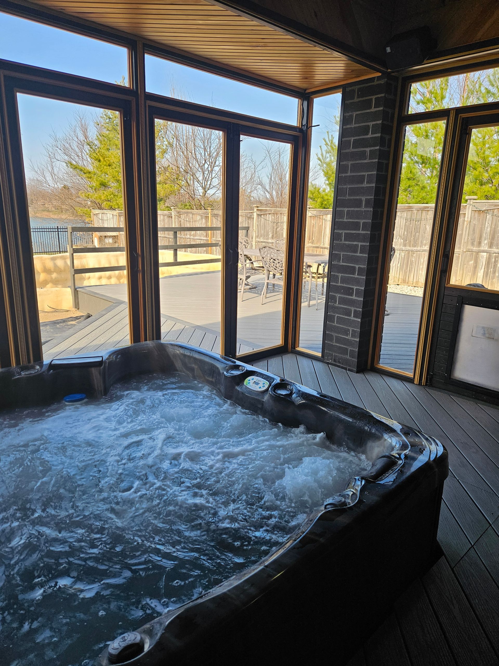 Hot tub in a sunroom with large windows overlooking a yard and fence. The water is bubbling.