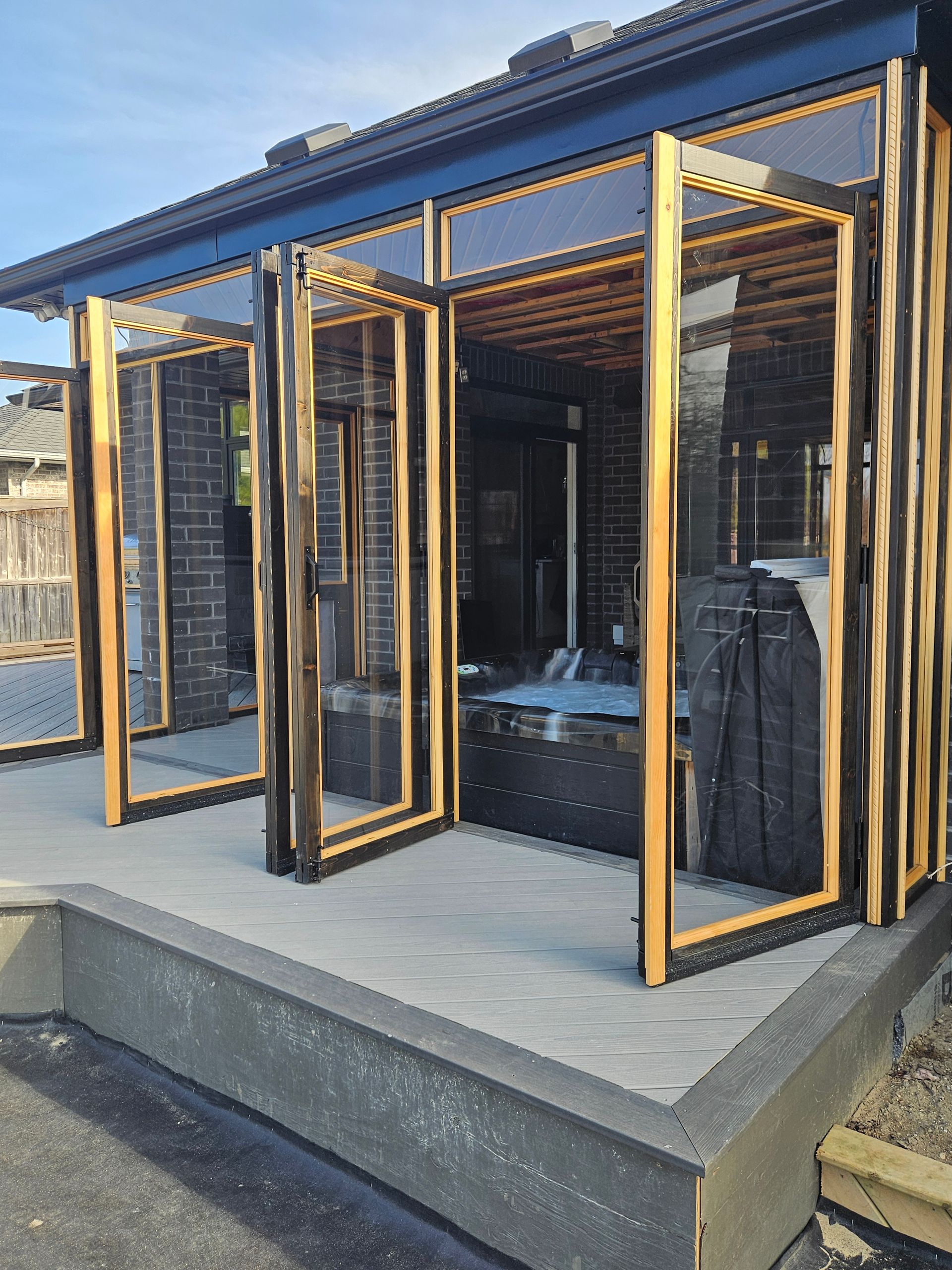 Bifold doors open to a spa inside a small, wooden-framed enclosure with a brick wall and paved floor.