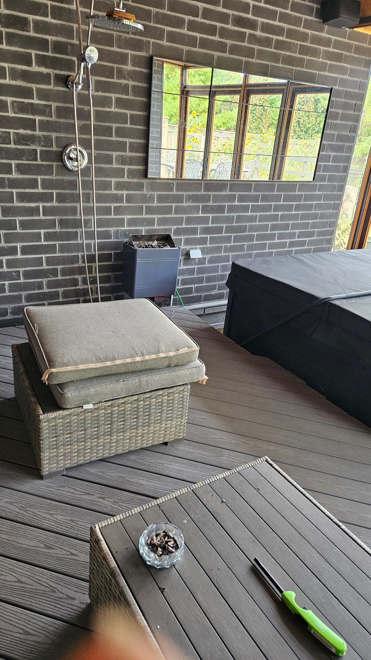 Outdoor lounge area with brick wall, shower, mirror, and wicker furniture.