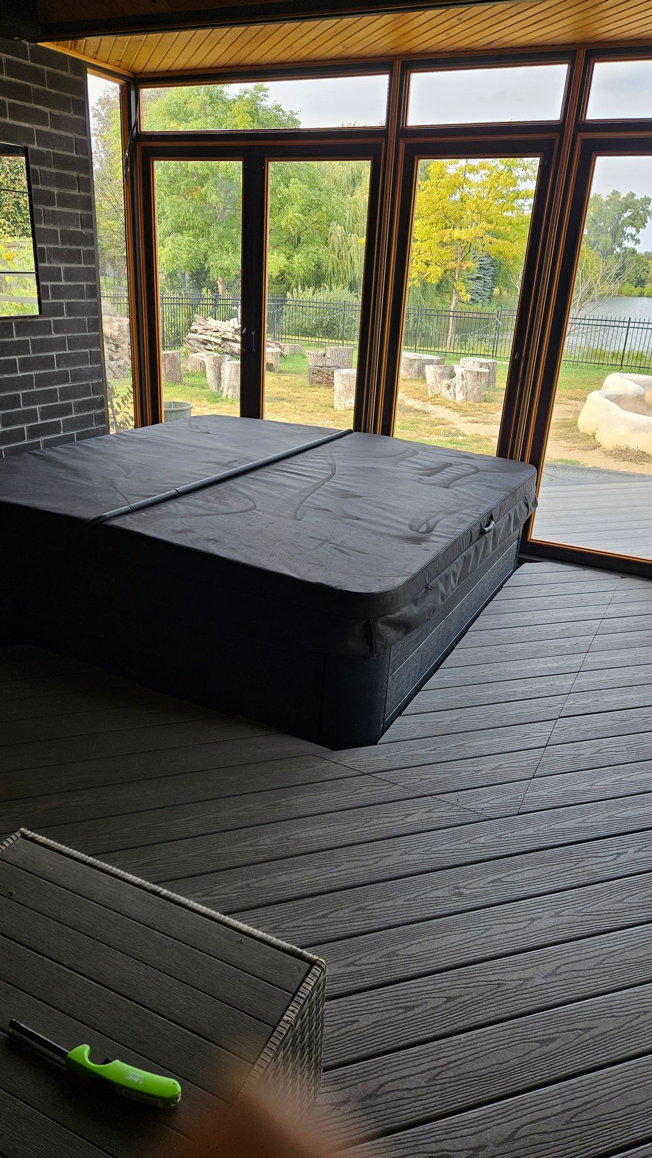 A black hot tub inside a room with large windows, overlooking trees and a body of water.