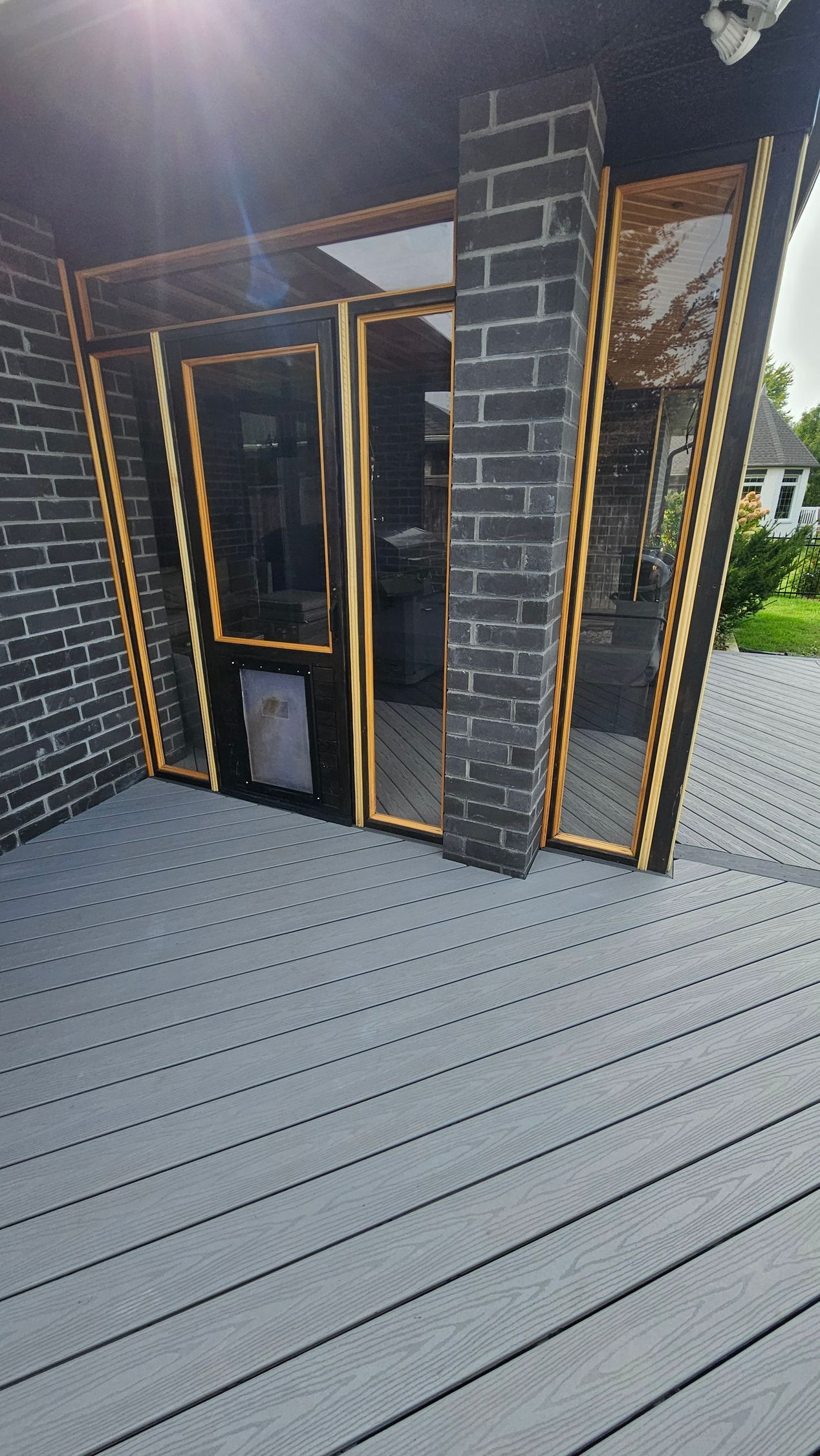 Exterior view of a building with dark brick facade and gold-framed windows/doors. Grey composite decking.