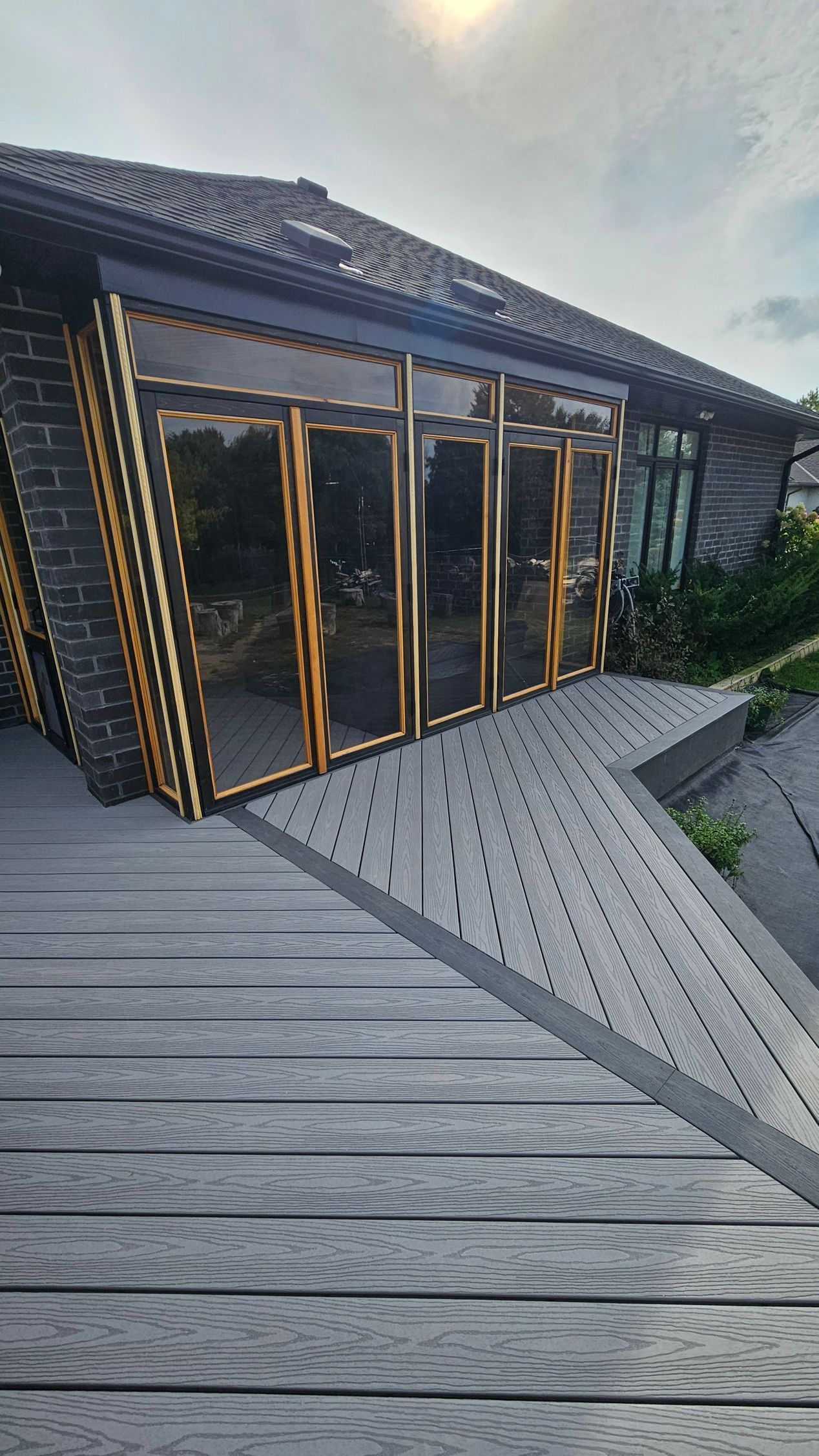 Exterior view of a building with glass doors and a gray wooden deck in sunlight.