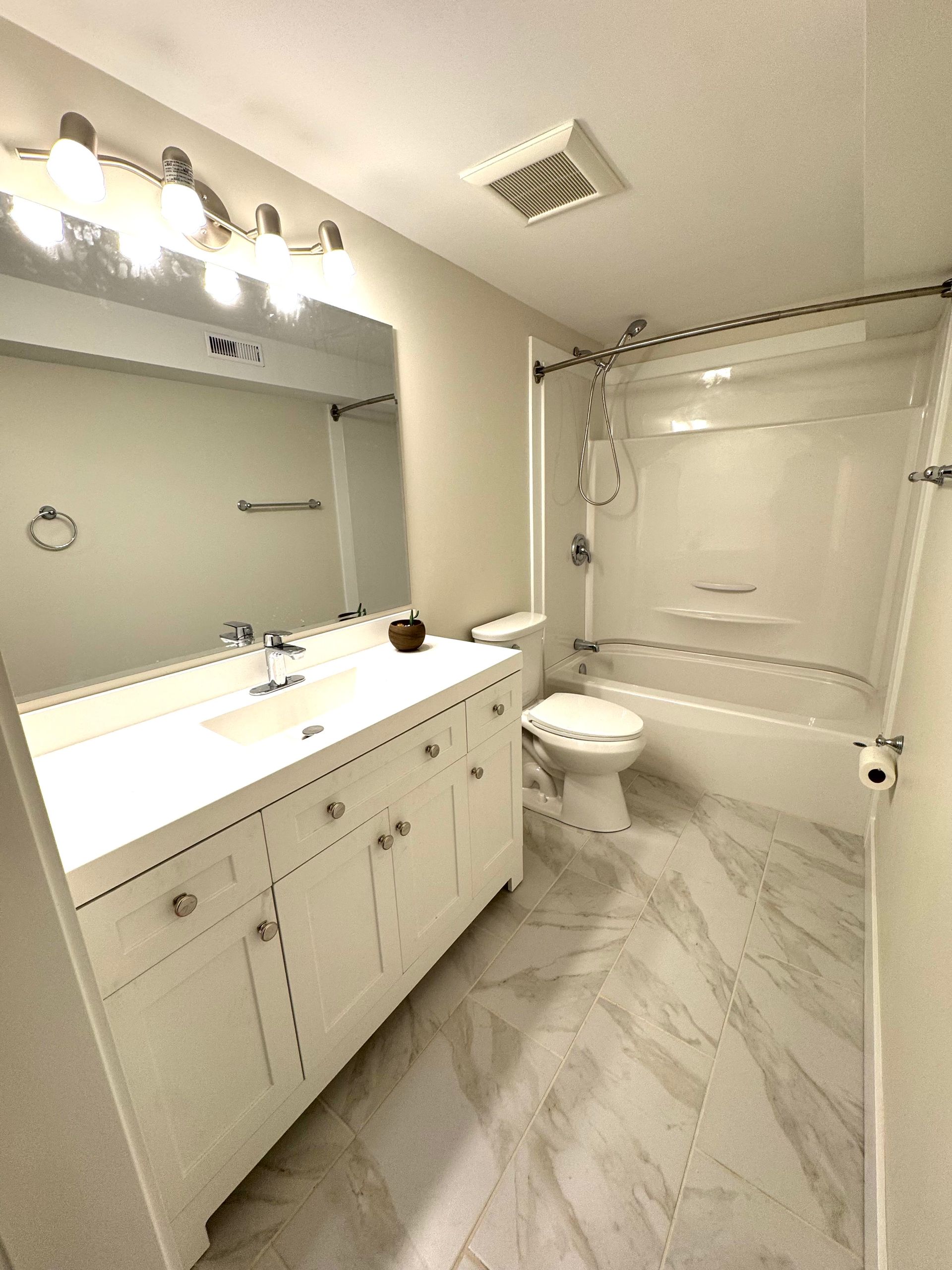 Bright bathroom with white vanity, large mirror, tub-shower combo, and herringbone tile floor.