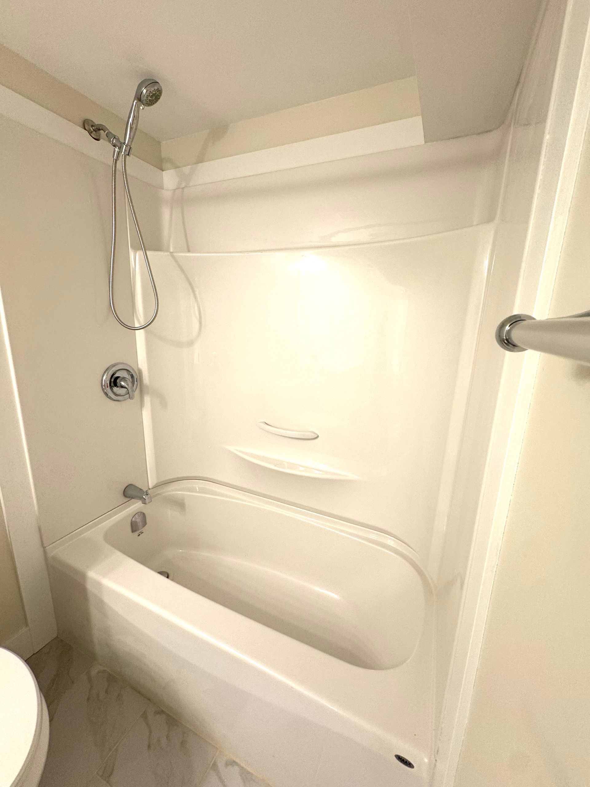 White bathtub and shower combo in a small bathroom with a handheld showerhead and curved tub ledge