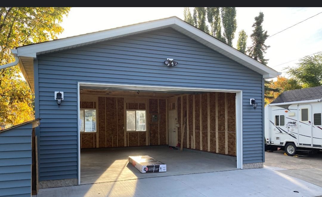 A garage with blue siding and an open door, showing unfinished wooden interior walls and two windows.