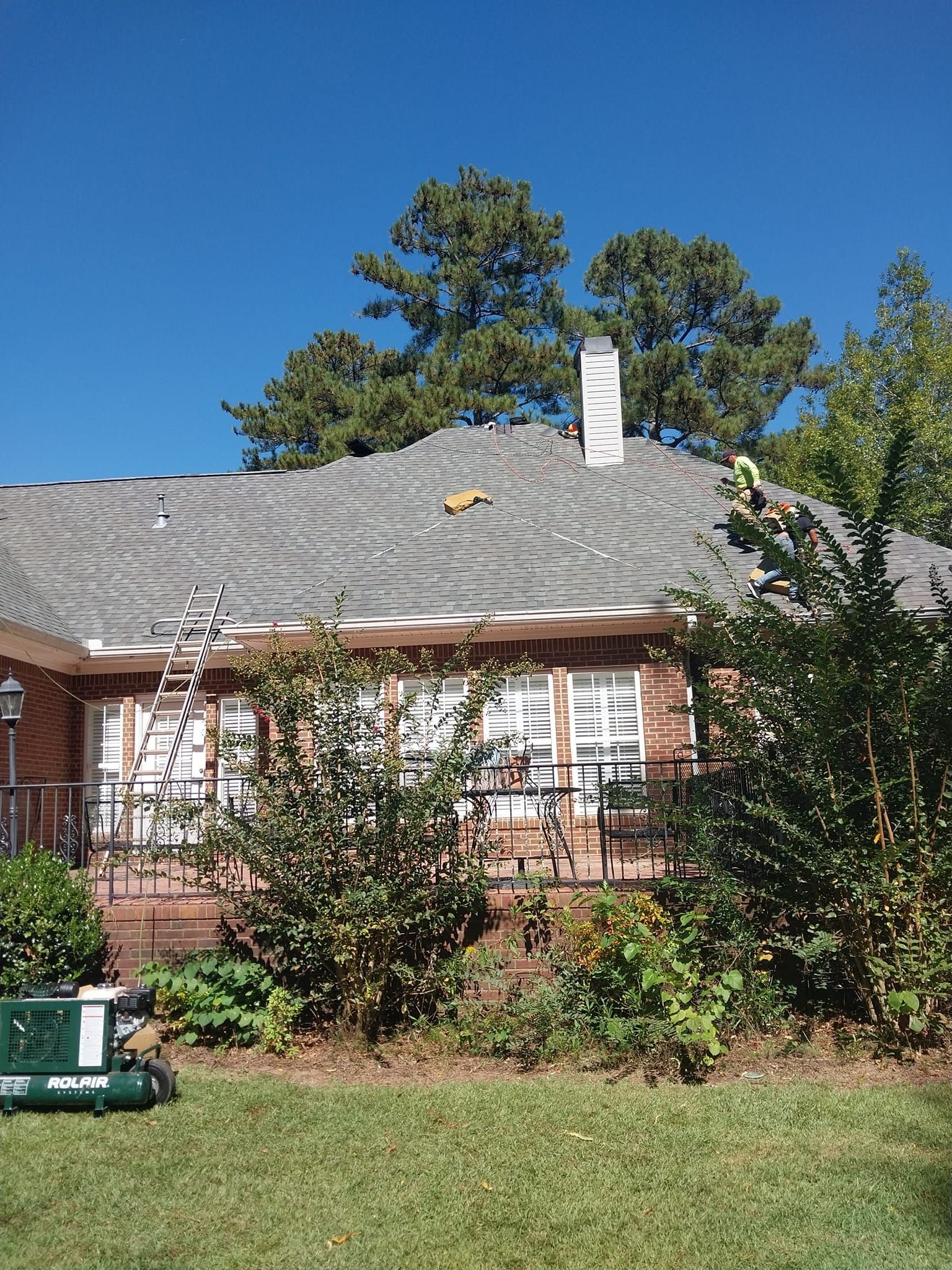 House exterior with roof under construction; ladder, chimney, and trees visible.