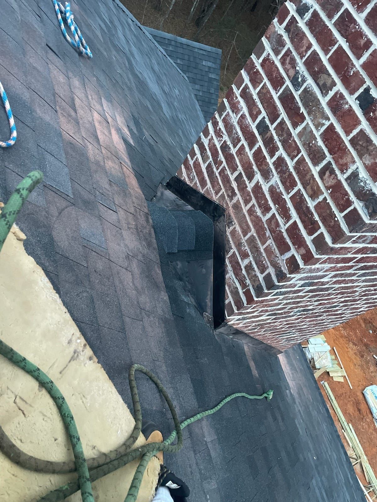 Roof with new shingles next to a red brick chimney; rope visible.