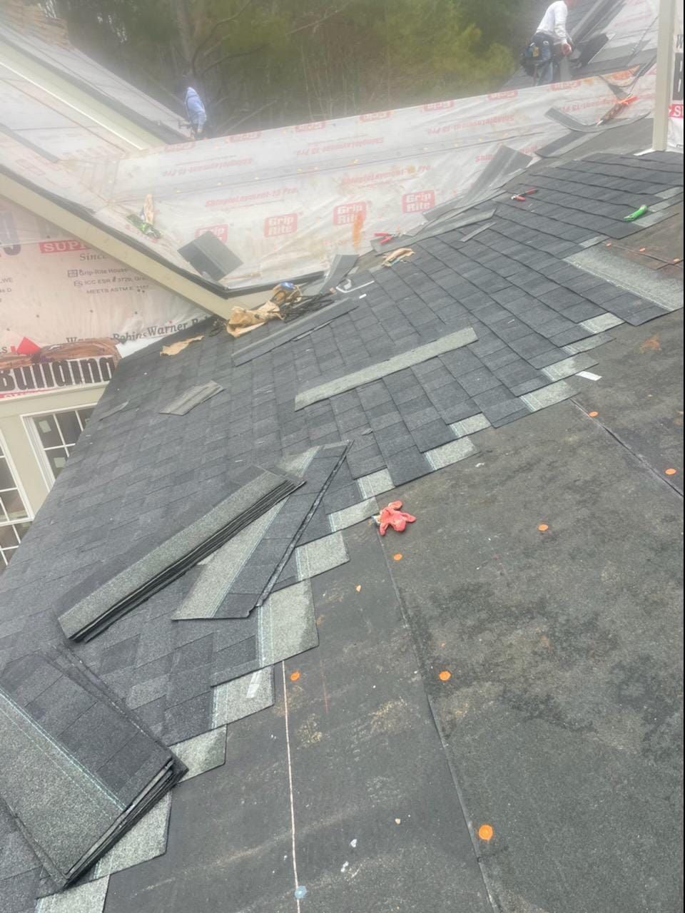 Roofers installing dark gray shingles on a roof, with some shingles partially laid and underlayment visible.