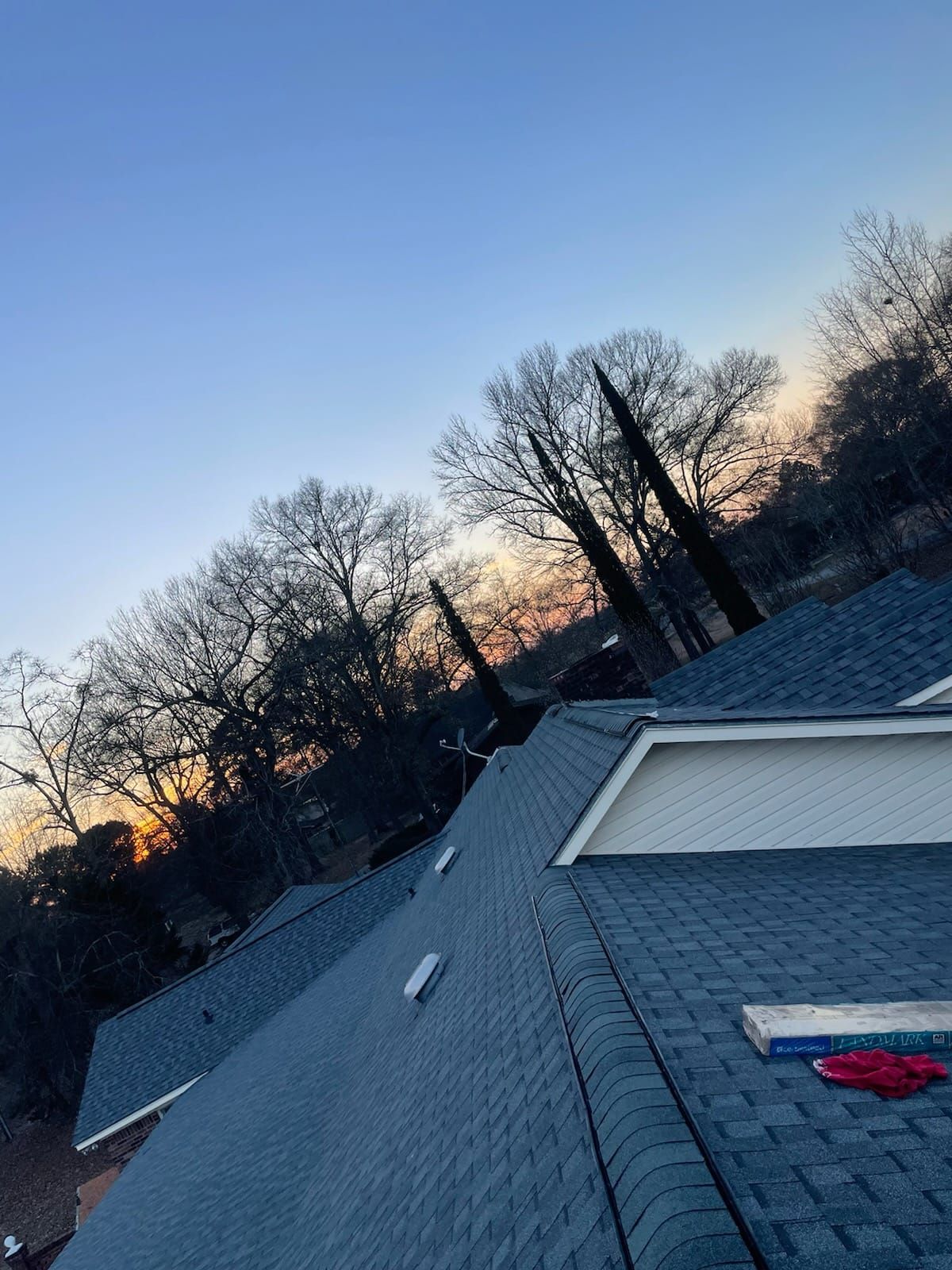 Newly shingled blue roof against a sunset sky, with trees in the background.