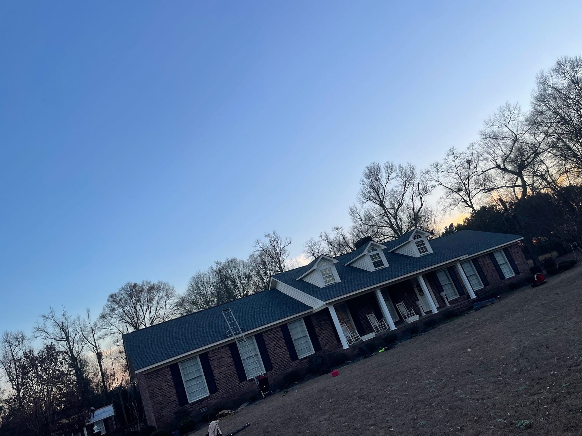 House with dark roof, brick facade, and porch, set against a blue sky with bare trees.