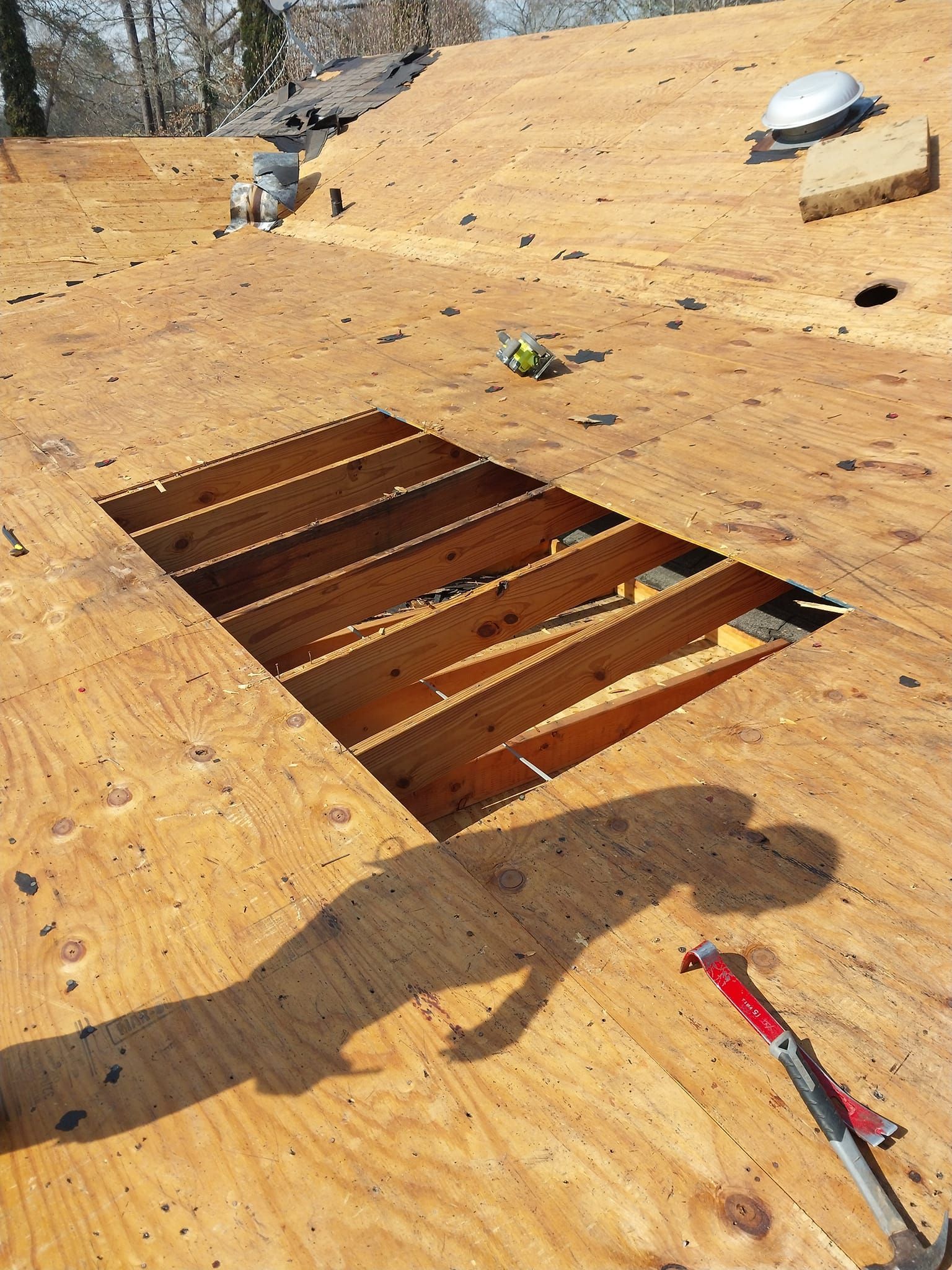Rooftop with a large rectangular opening, showing wooden beams. Tools and a shadow of a person are present.