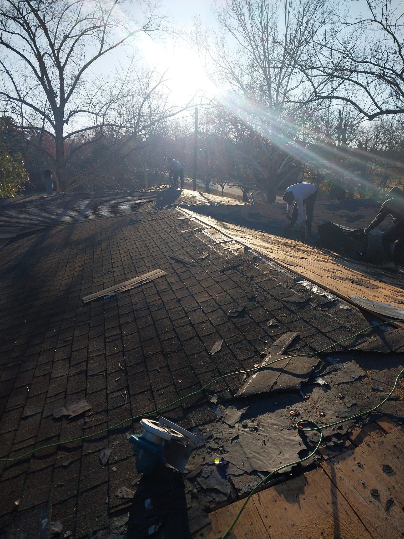 Workers removing old shingles from a roof on a sunny day.