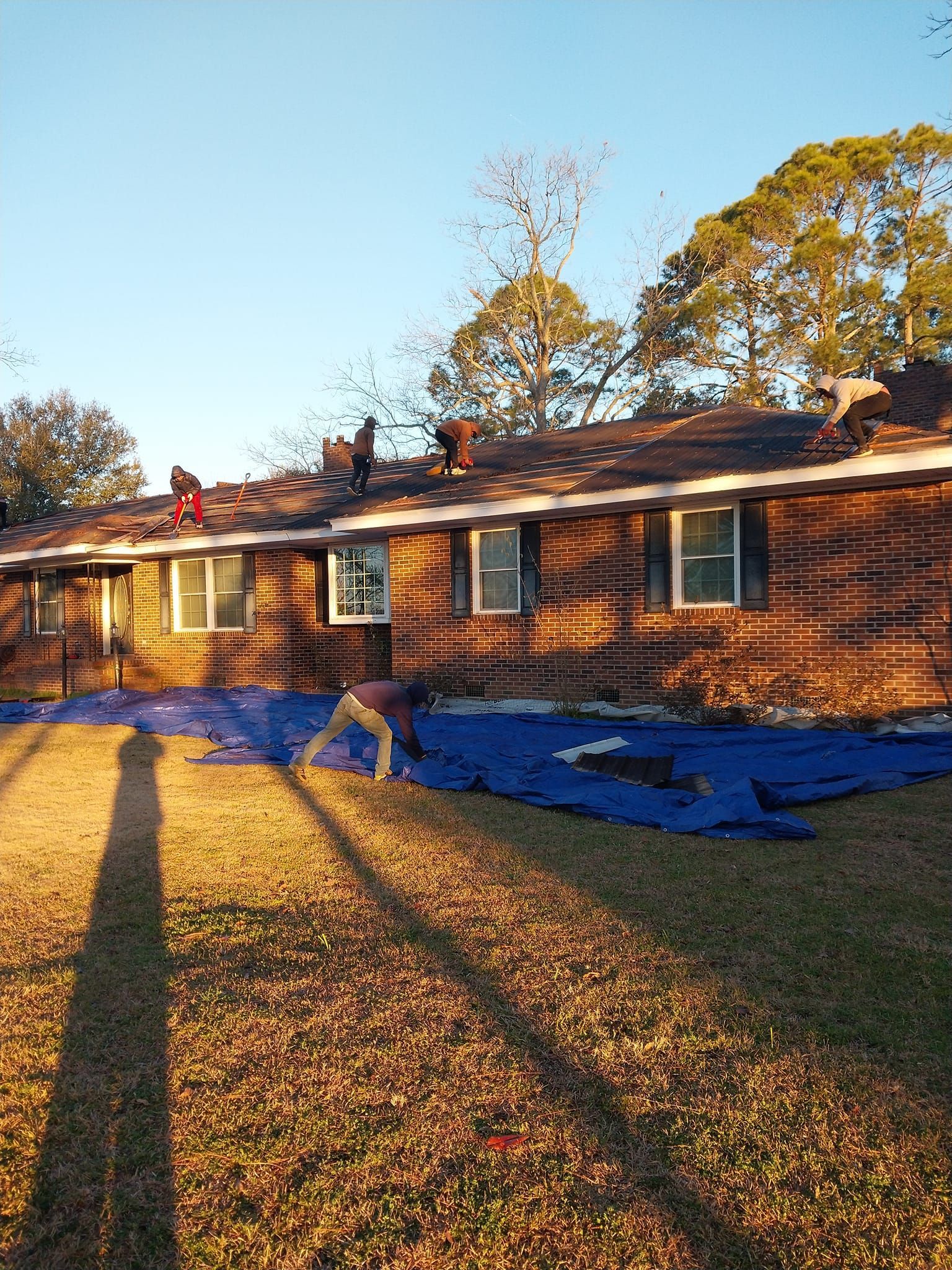 Roofers working on a house, covered in blue tarps, sunny day.