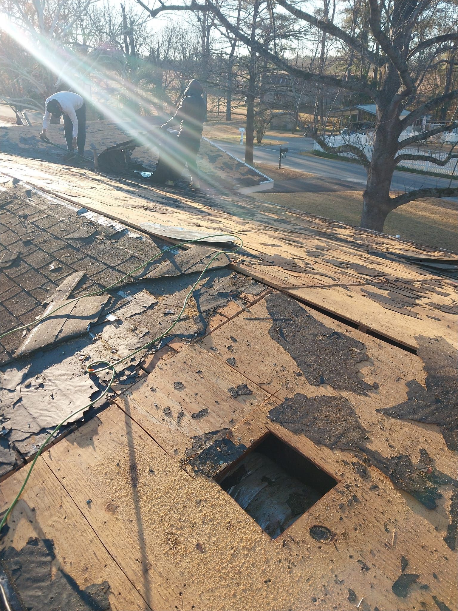 Damaged roof with worker in background; sun shining through trees; burnt landscape.