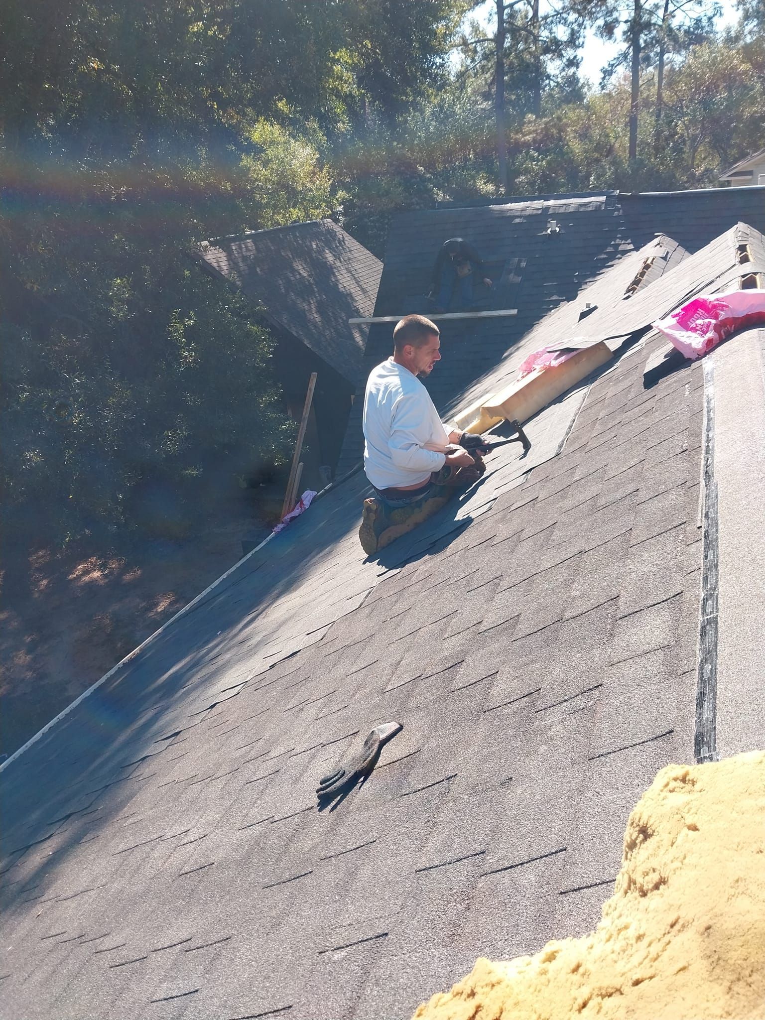 Person on a roof working with roofing materials; outdoor setting, sunny.