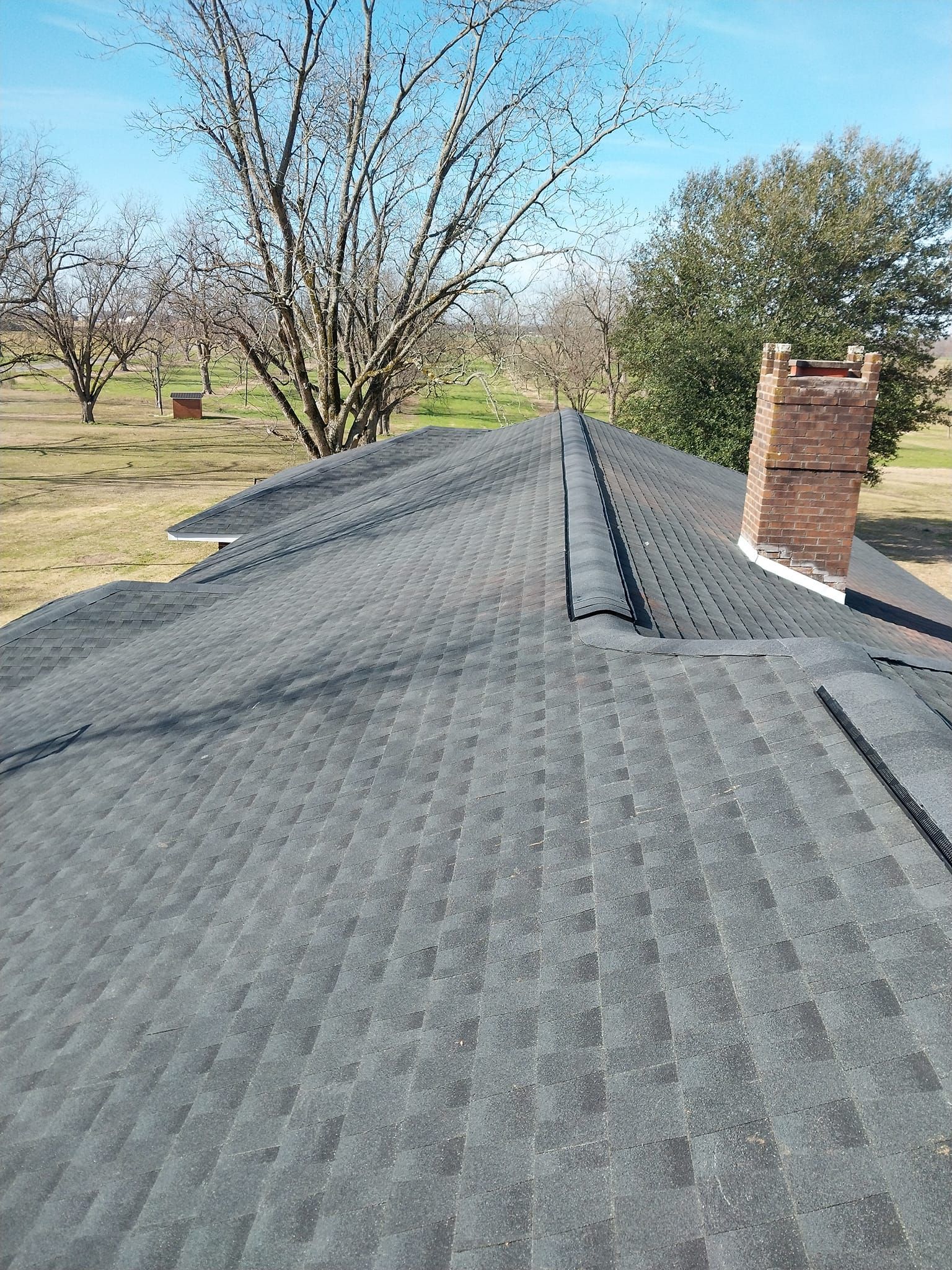 Dark gray asphalt shingle roof with a brick chimney and trees in the background.