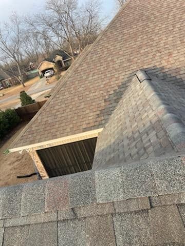 Overhead view of a house roof with brown and gray shingles. A triangular section protrudes.