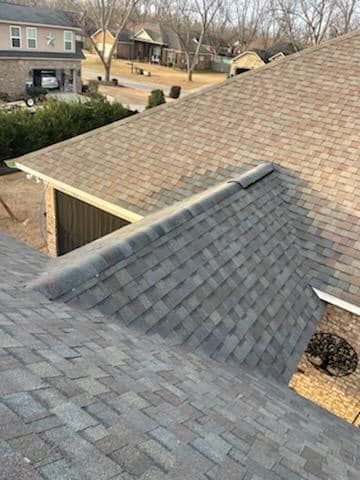 Gray and brown shingled rooftops, with a dark cap at the roof's ridge, and a glimpse of the surrounding neighborhood.