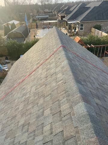 Overhead view of a gray shingle roof with a red rope along the ridge, set in a neighborhood.