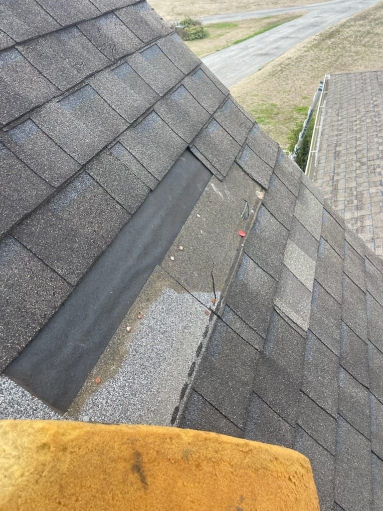 Close-up of asphalt shingles on a roof with a section of missing shingles, showing the underlayment.