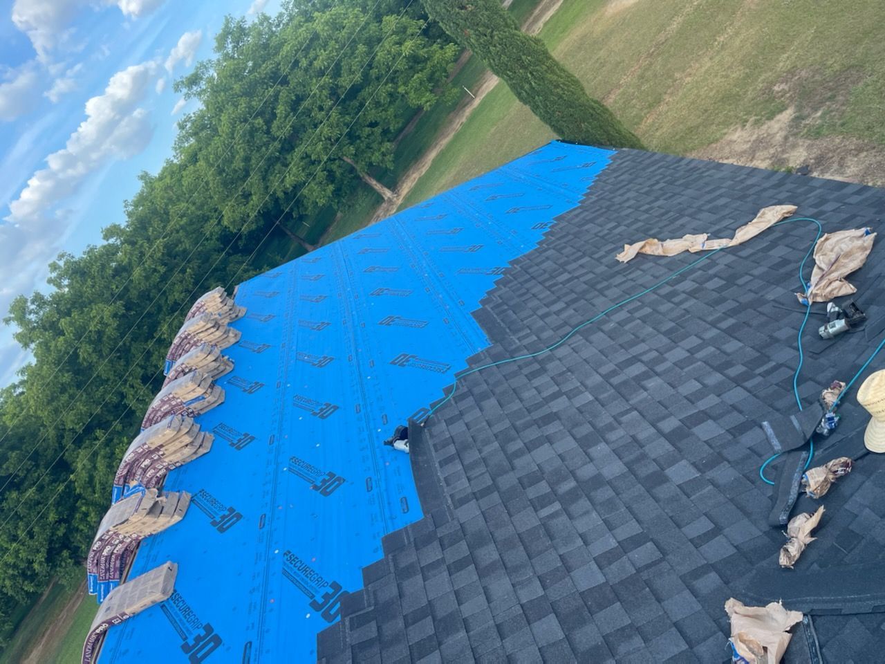 Roof partially covered with black shingles and blue underlayment; construction site.