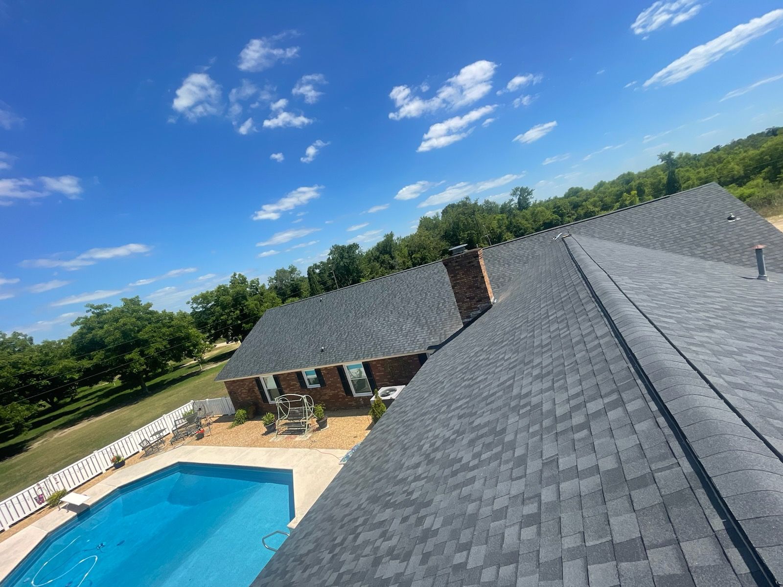 Blue-roofed house with a swimming pool, trees, and blue sky with some clouds.