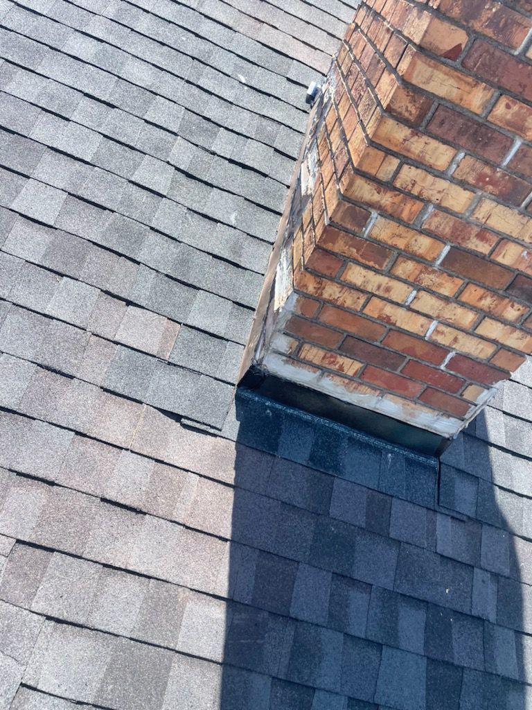 Roof with chimney; shingles showing wear near the brick structure; a dark shadow is cast.
