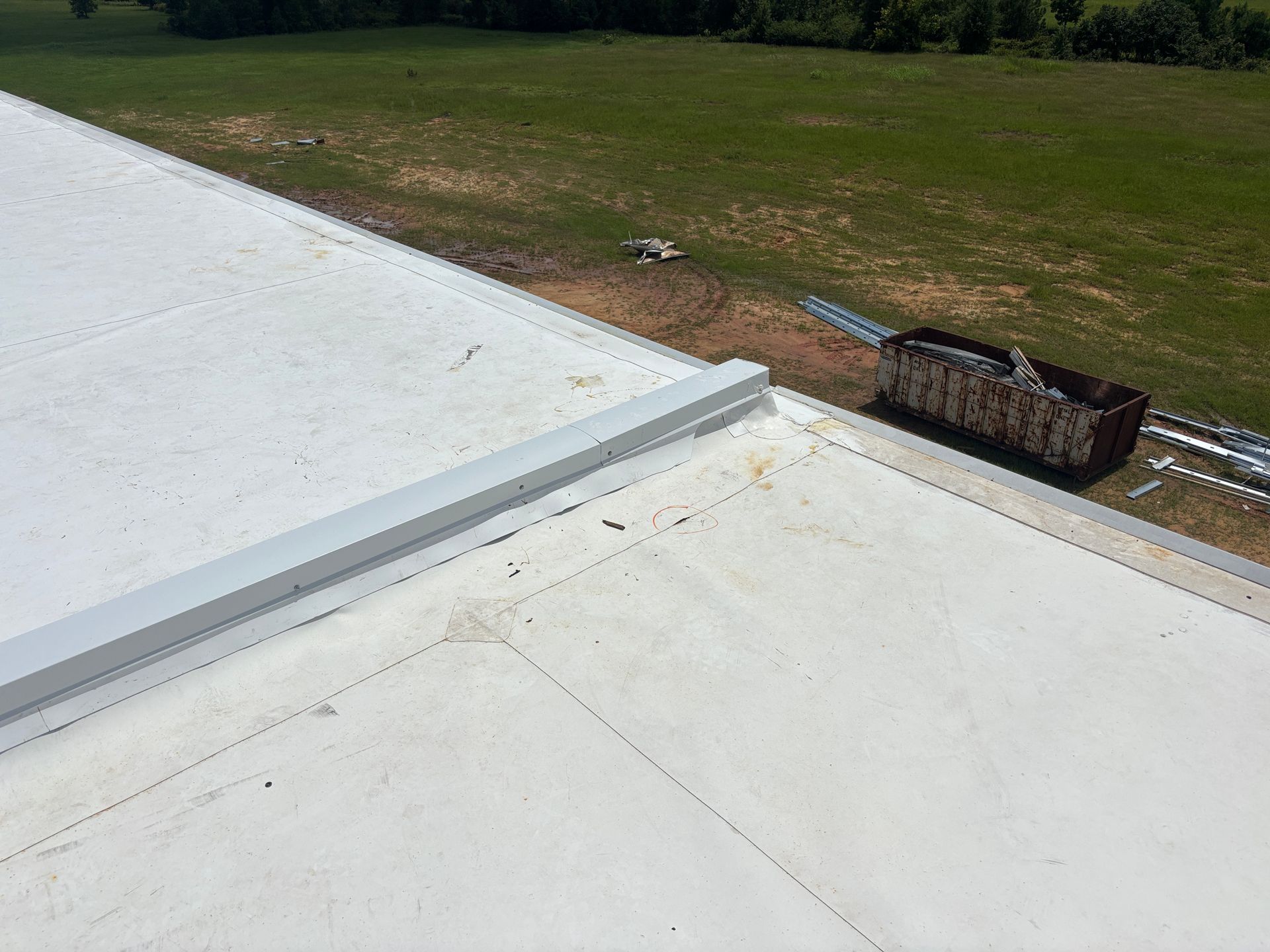 A flat, white roof with a metal edge; a grassy field and dumpster are visible in the background.