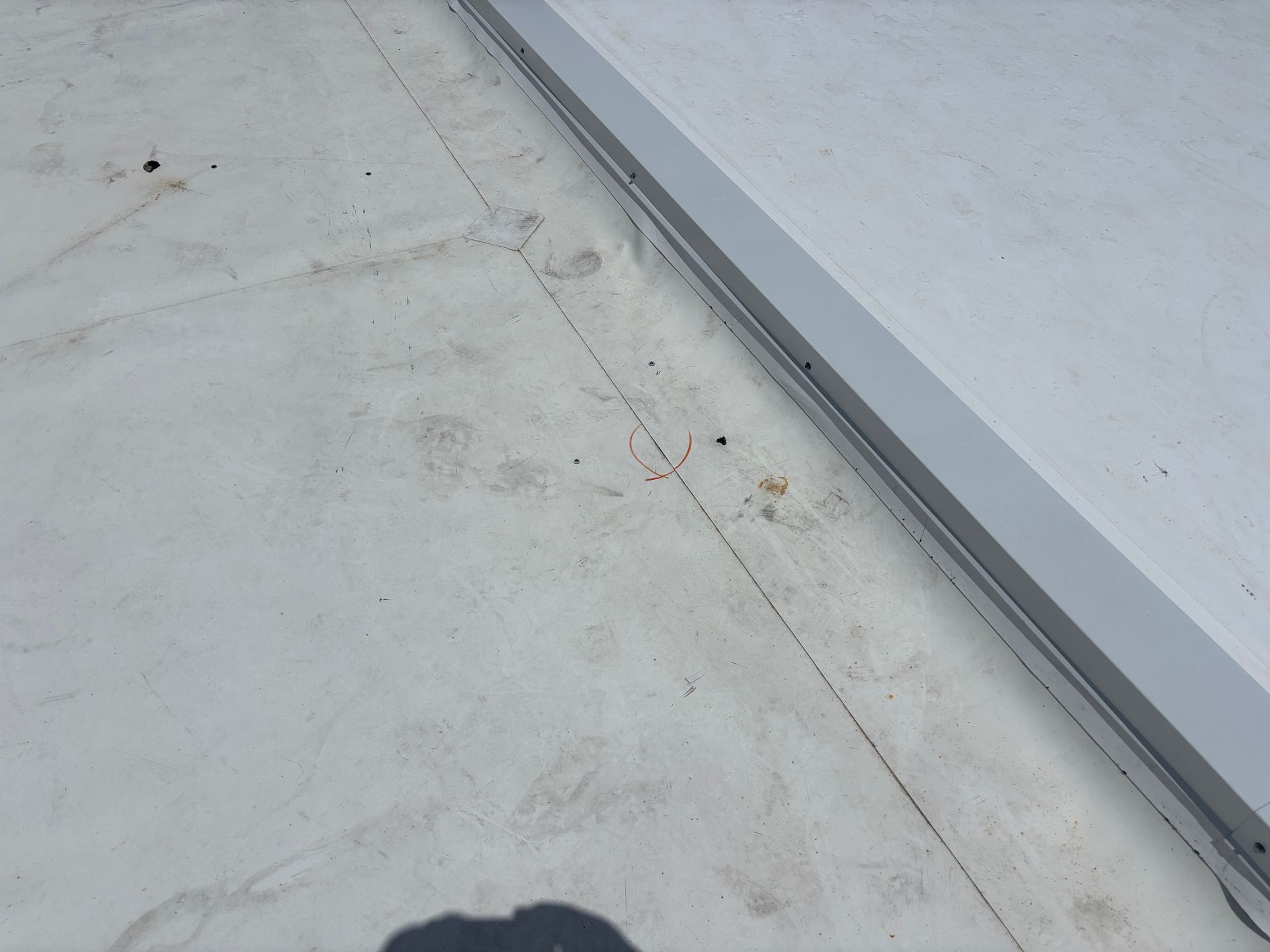 White flat roof surface with a seam, near a white edge. Small debris scattered.