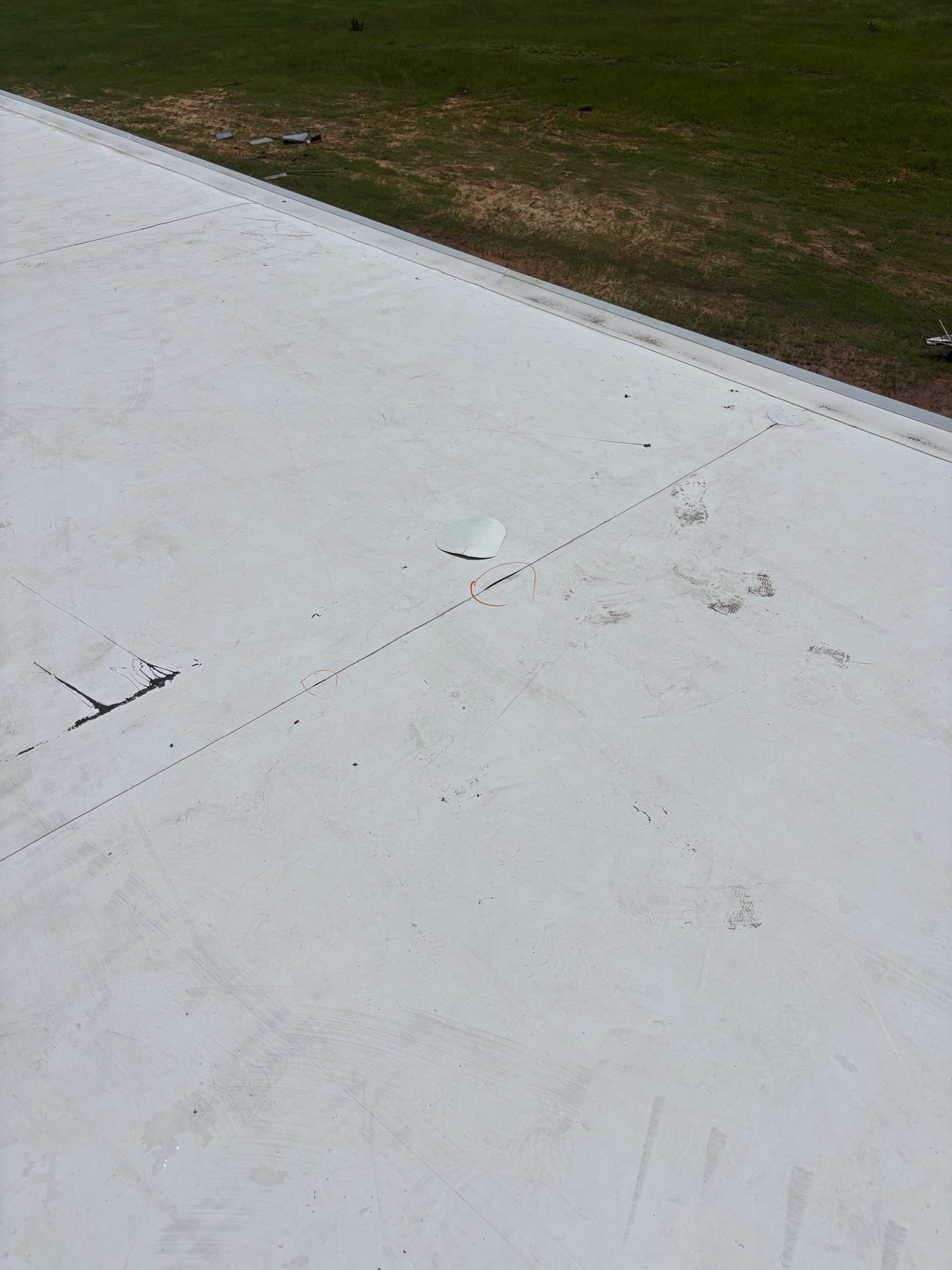White airplane wing with rivets and ground in the background.