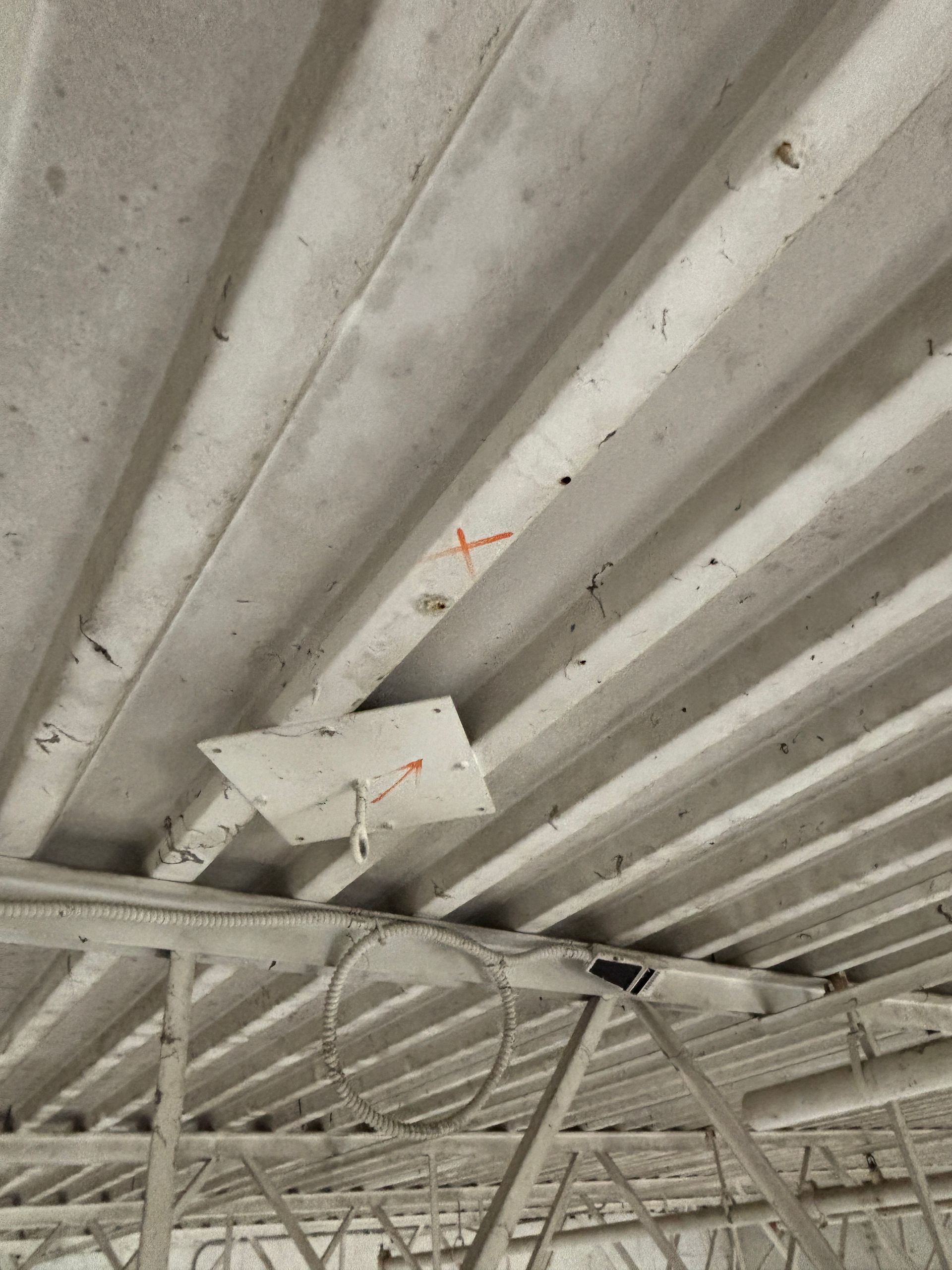 Gray, ribbed concrete ceiling with a metal bracket and wire below. Red Xs mark areas on the concrete.