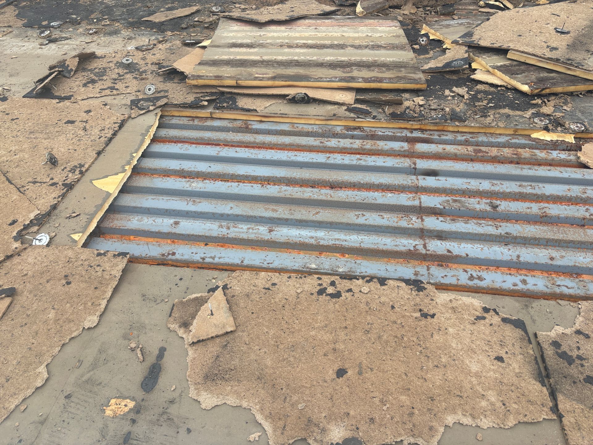 Damaged roofing, with torn asphalt shingles and exposed corrugated metal sheets.