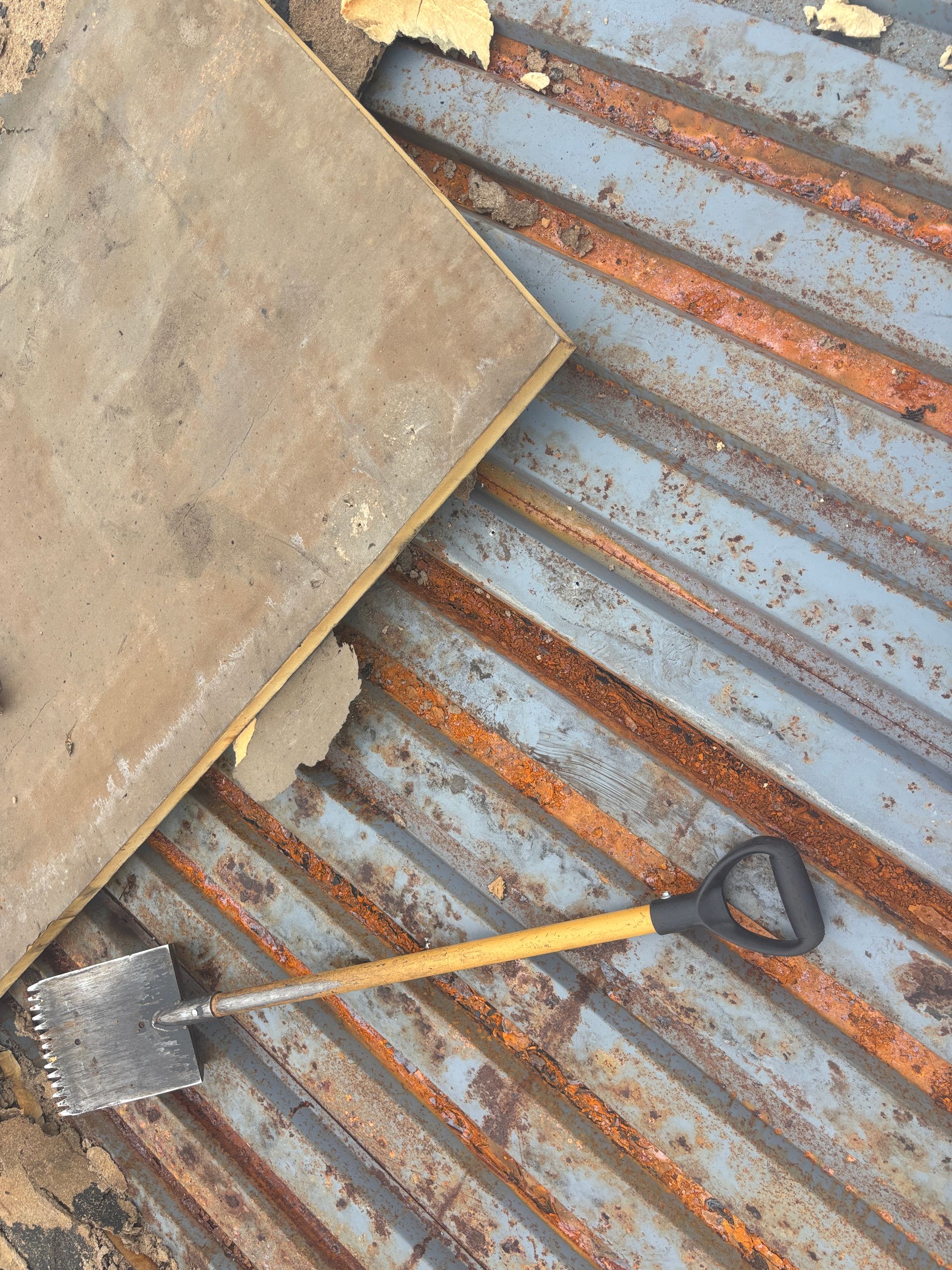 Shovel and a rectangular object on a rusted, corrugated metal surface.
