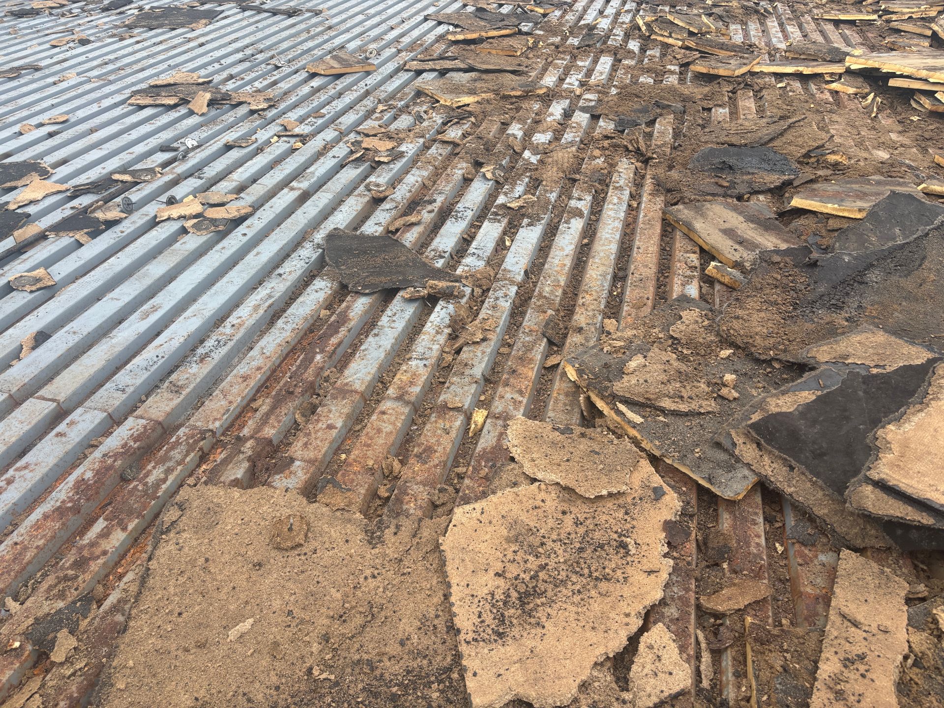 Debris and roofing material on corrugated metal roof. Brown and gray hues.