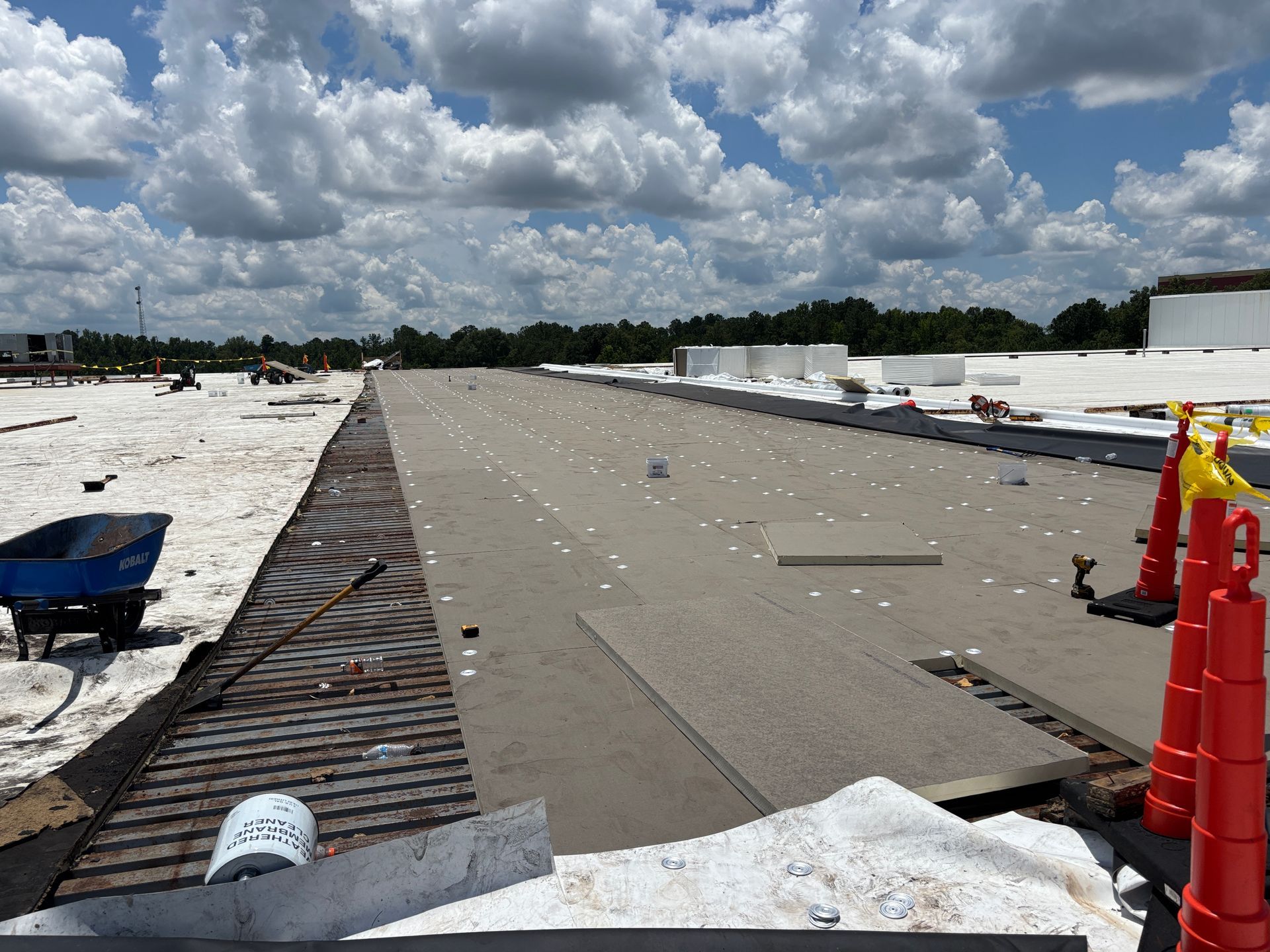 Rooftop under construction on a sunny day. Workers and materials visible; cloudy sky overhead.