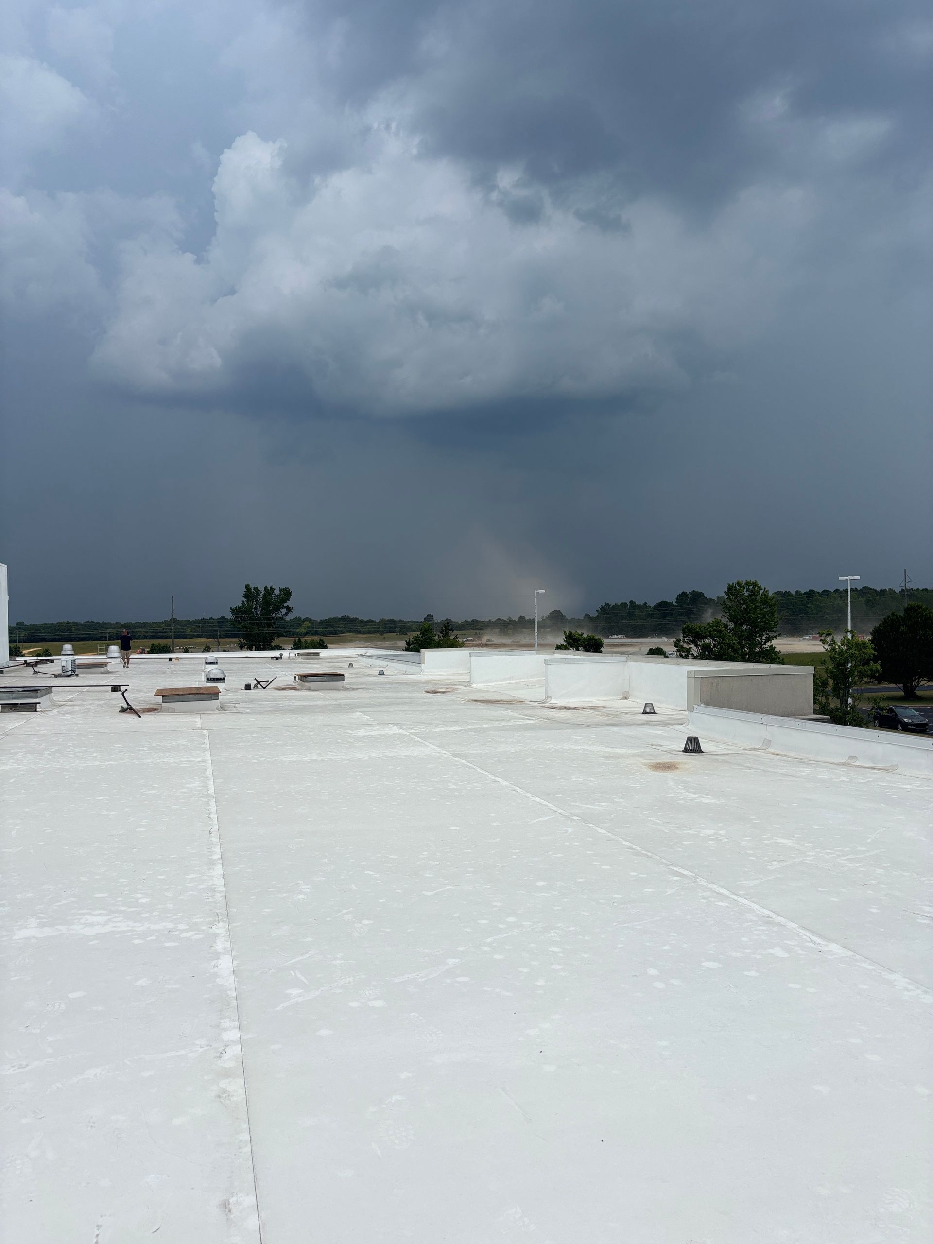 Overcast sky with dark clouds and rain over a distant, flat landscape. White rooftop in the foreground.