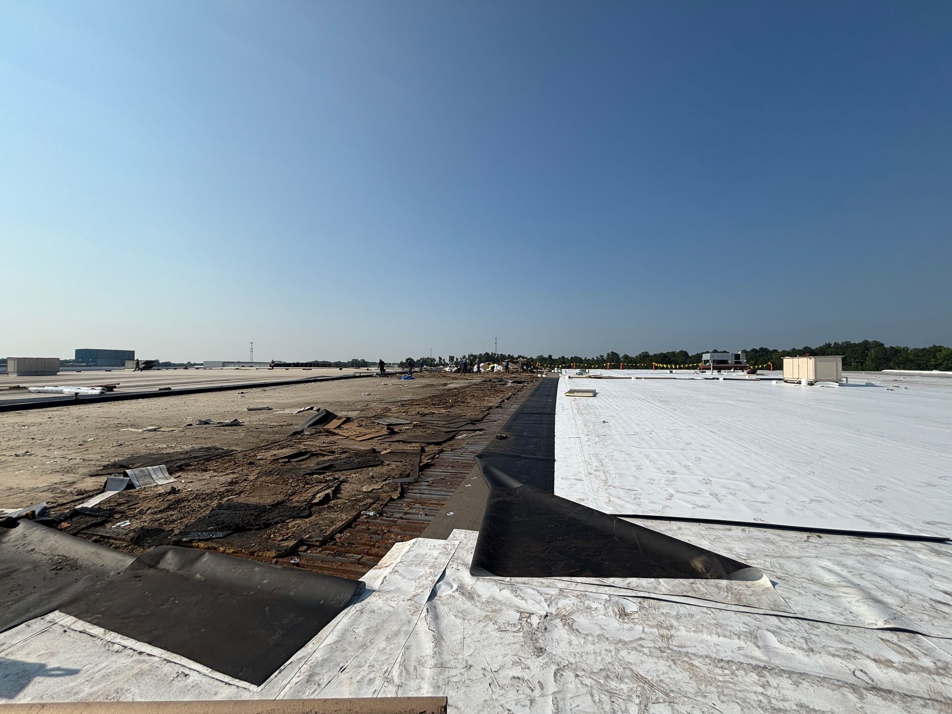 A construction site with a freshly laid, white roof and exposed dirt under a clear blue sky.