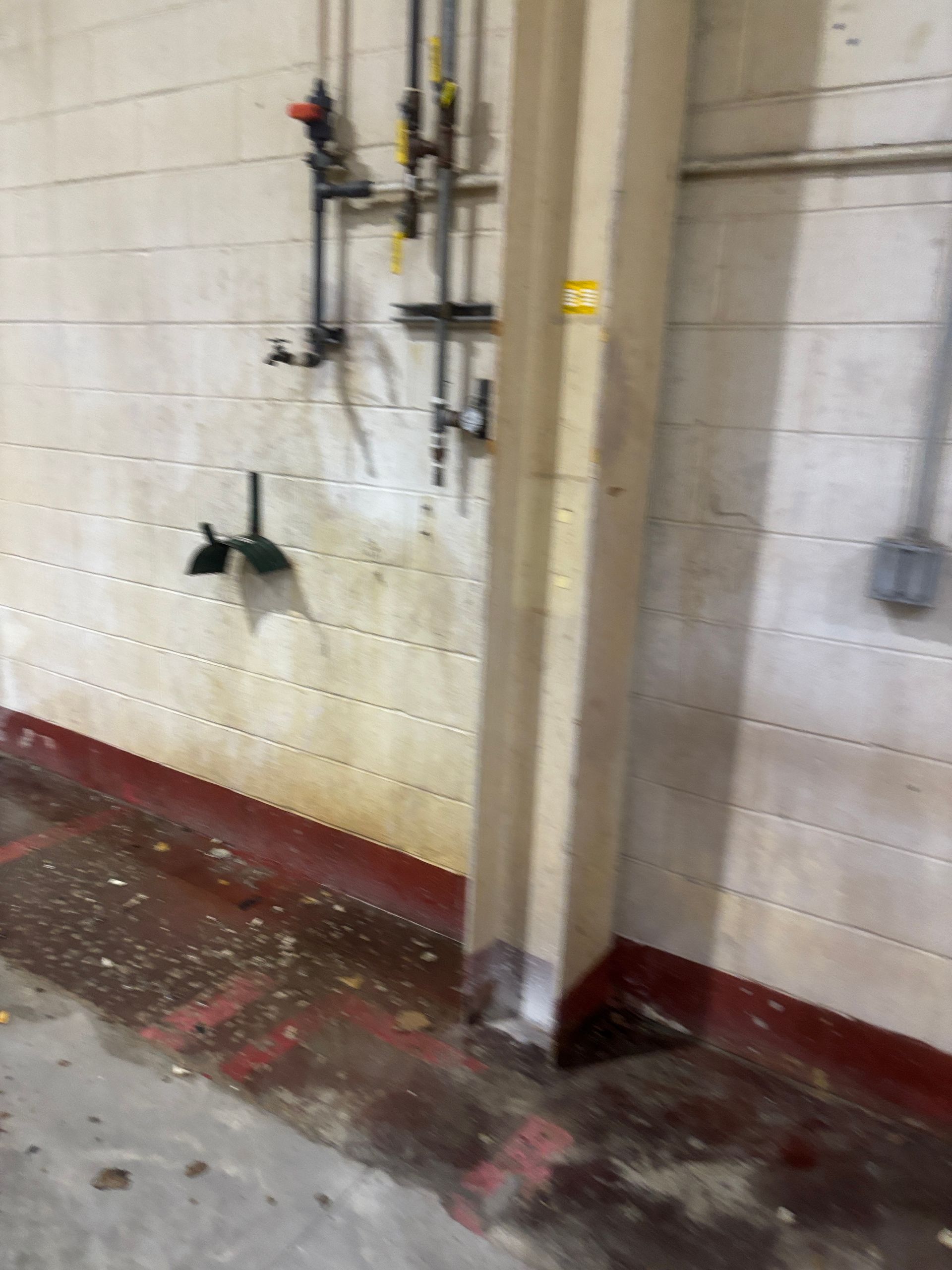Concrete industrial space: red-trimmed floor, water stain on wall, pipes, concrete column, and electrical outlet.