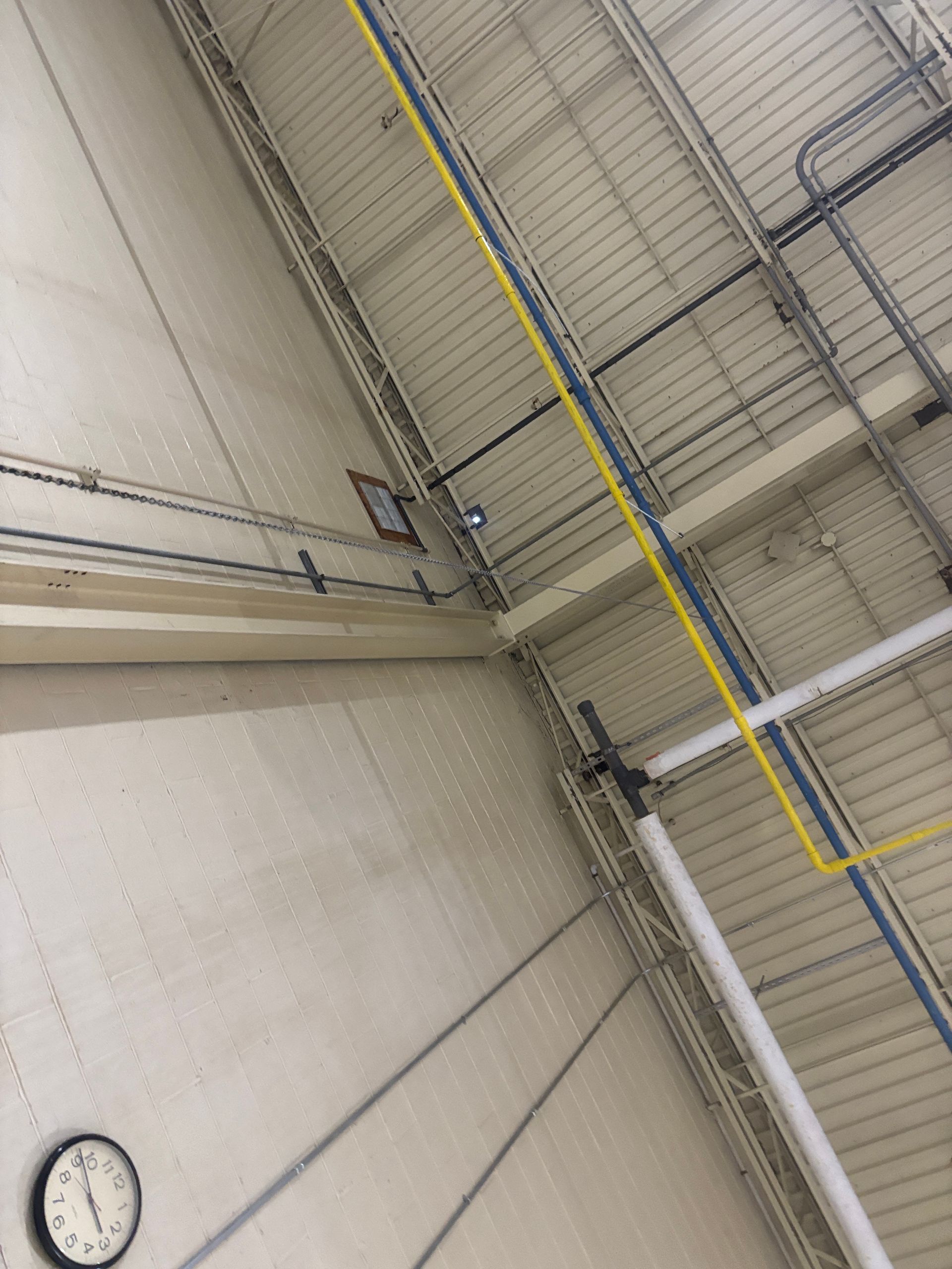 High-angle view of a beige industrial interior. Exposed pipes and wiring run along the ceiling.