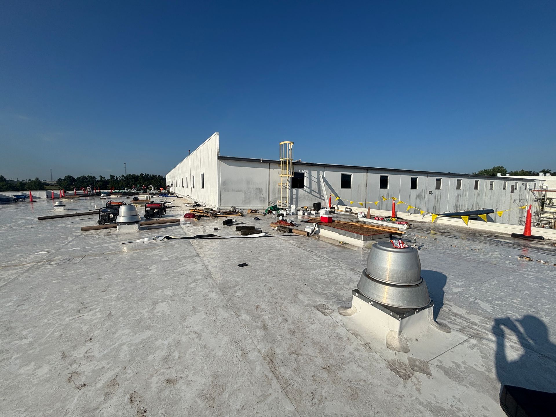 Rooftop with debris, vents, and a low building under a blue sky.