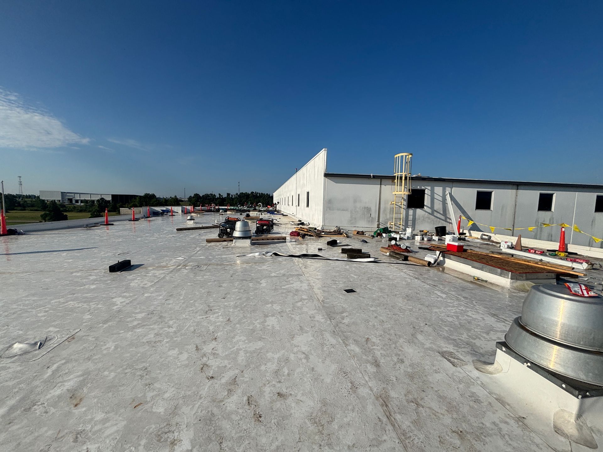Workers on a flat roof with tools and debris, white building in the background, blue sky.