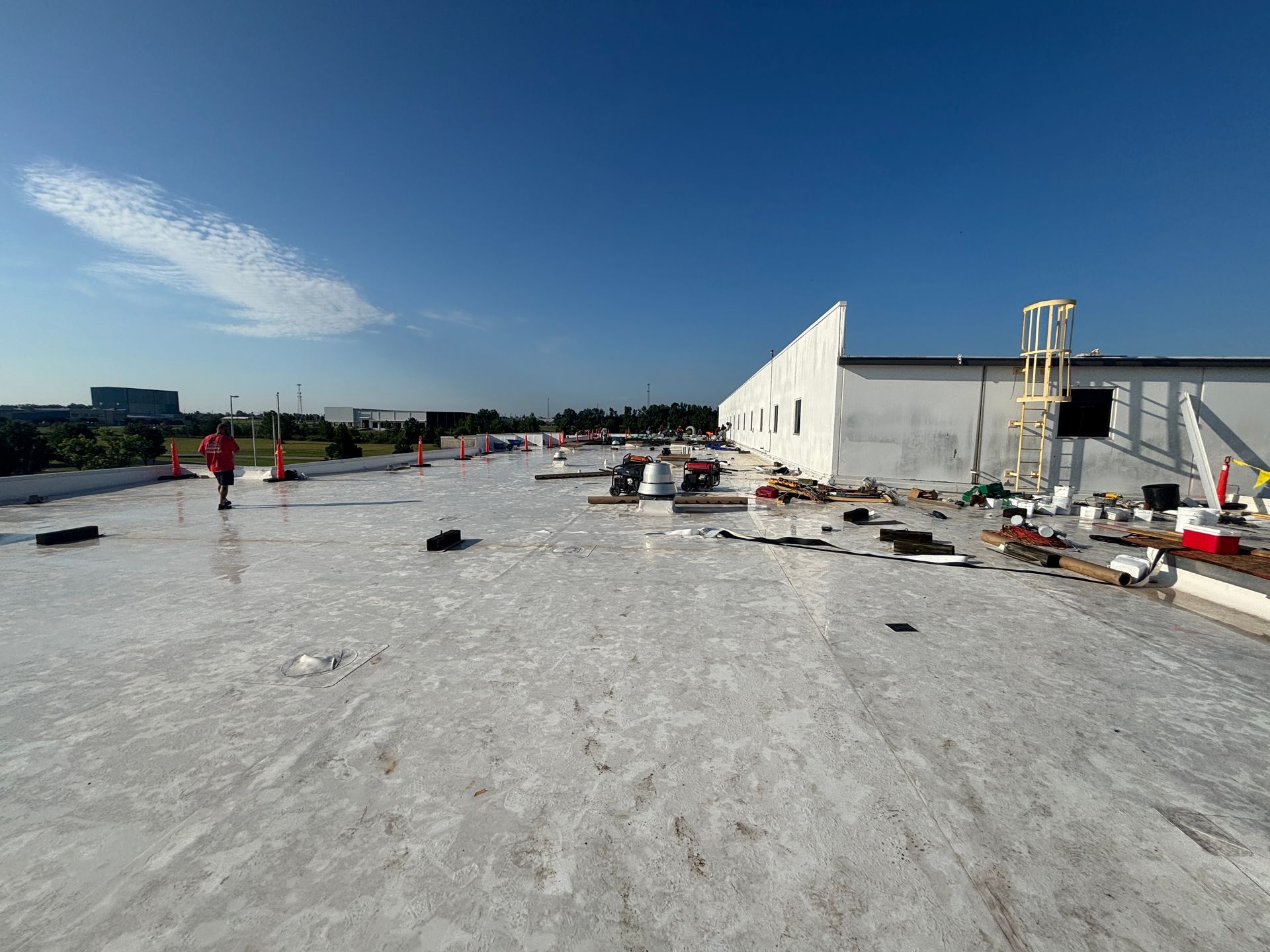 Workers on a flat roof with materials, building in progress, bright blue sky.