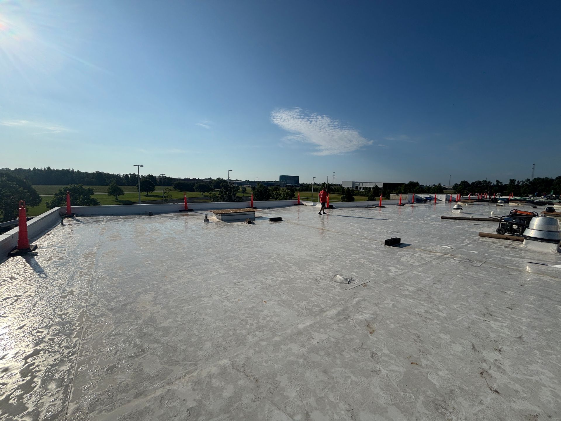 Flat, white roof with construction cones, trees, and a clear blue sky.