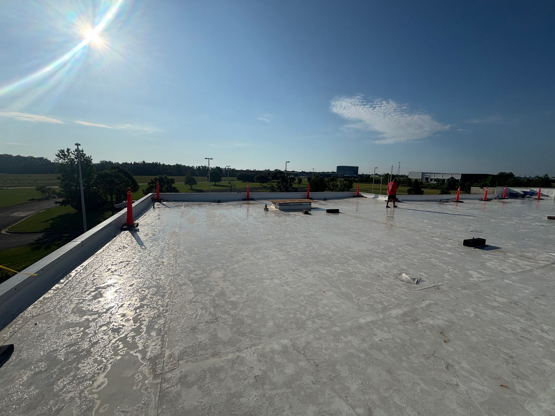 A rooftop with a white reflective surface, under a bright sun, orange cones line the edge.