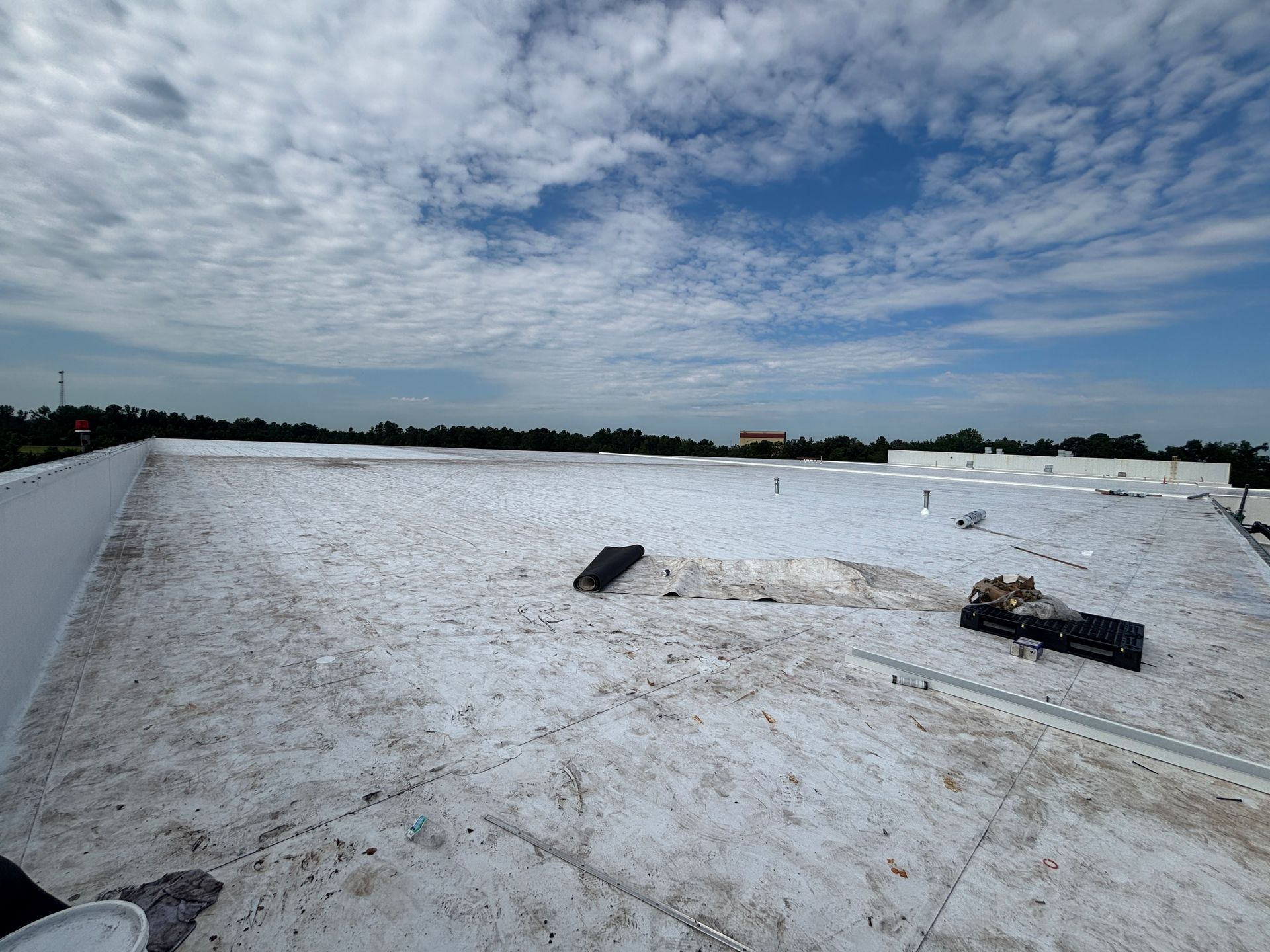 Flat white commercial roof under a partly cloudy blue sky. Debris scattered across the surface.