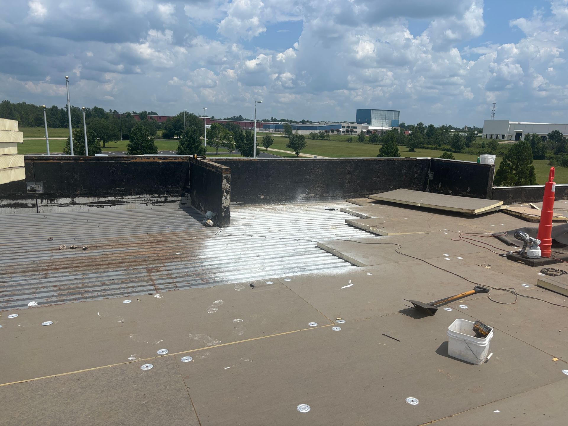 A flat commercial roof under construction with white foam insulation being applied on a sunny day.