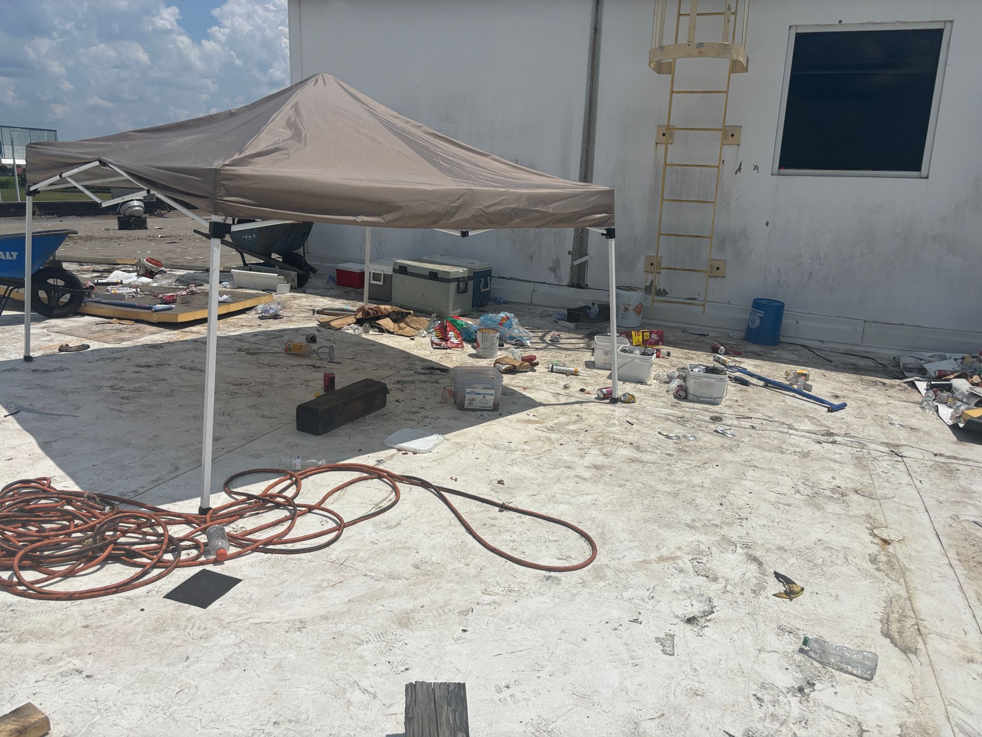 Construction site with tan canopy, tools, and materials. White building with ladder.