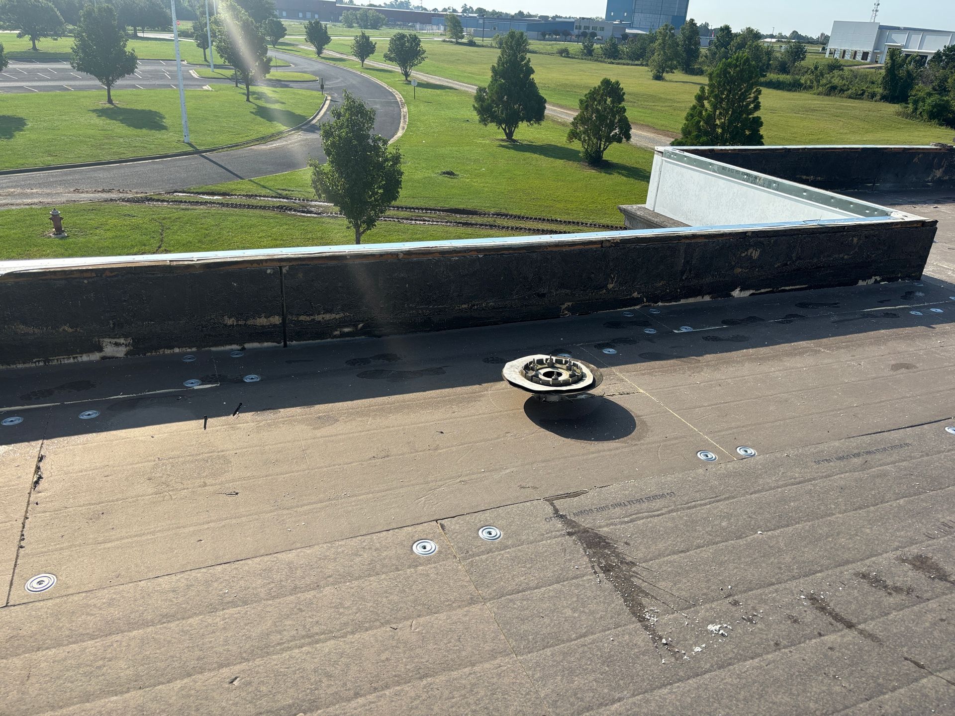 Flat roof with a drain, near a low wall with green space in the background.