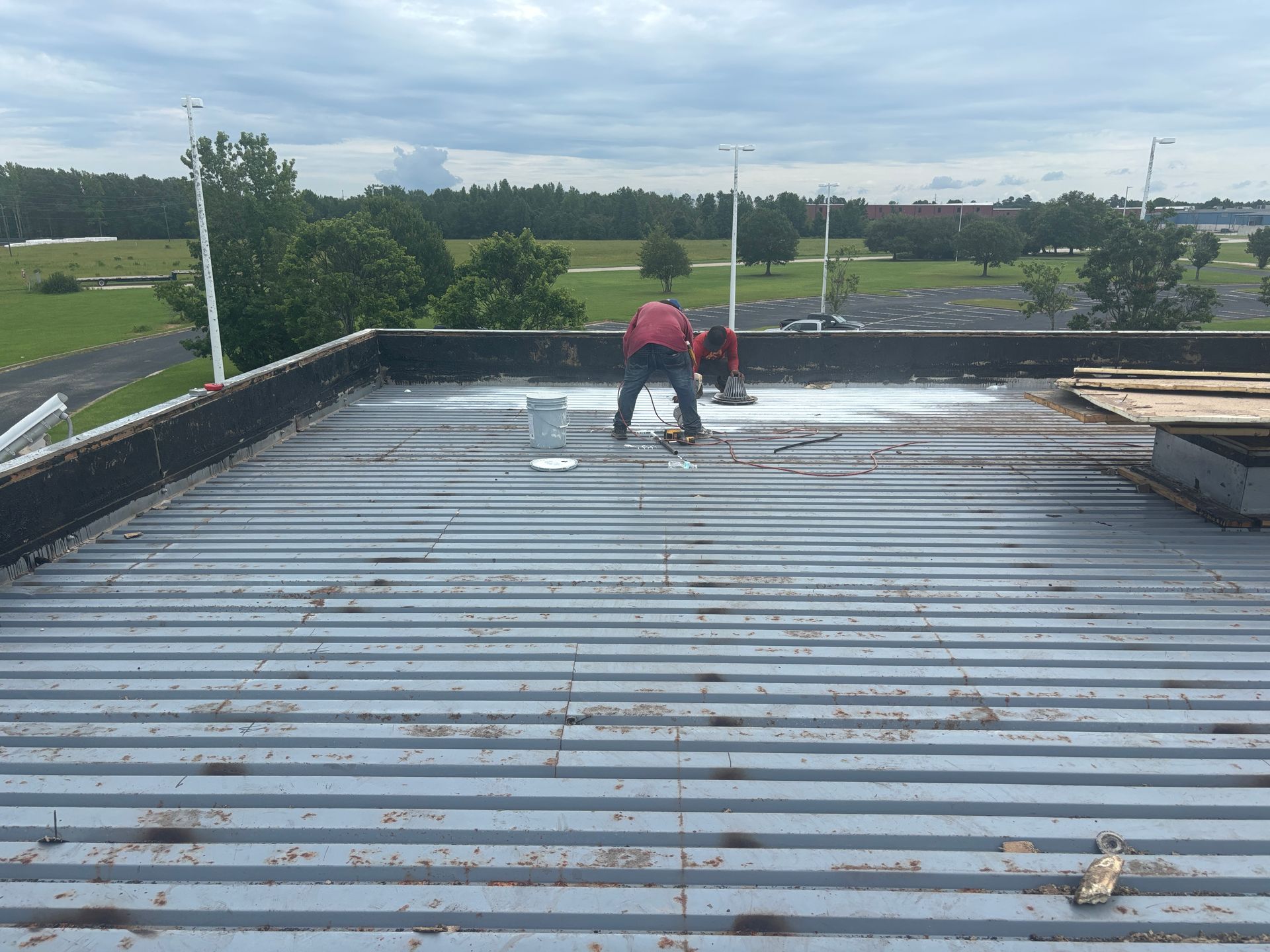 Two people painting a metal roof white on a cloudy day, with a golf course in the background.